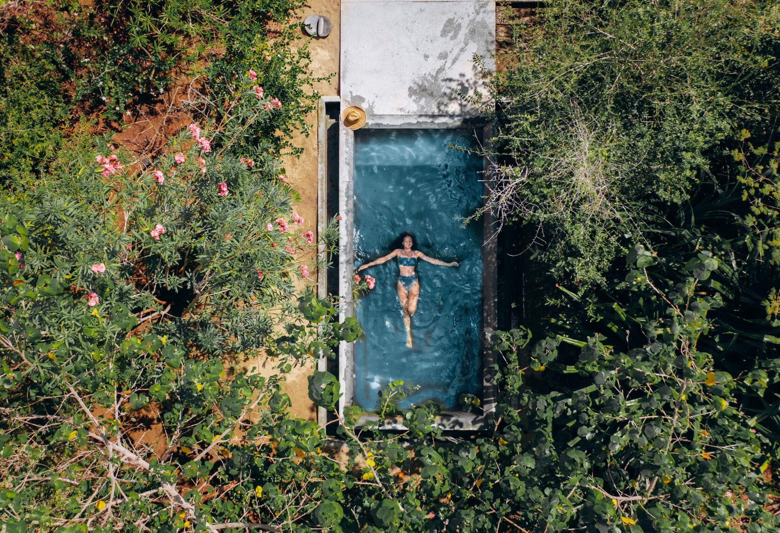 A woman swims on her back in a small pool surrounded by lush plants.