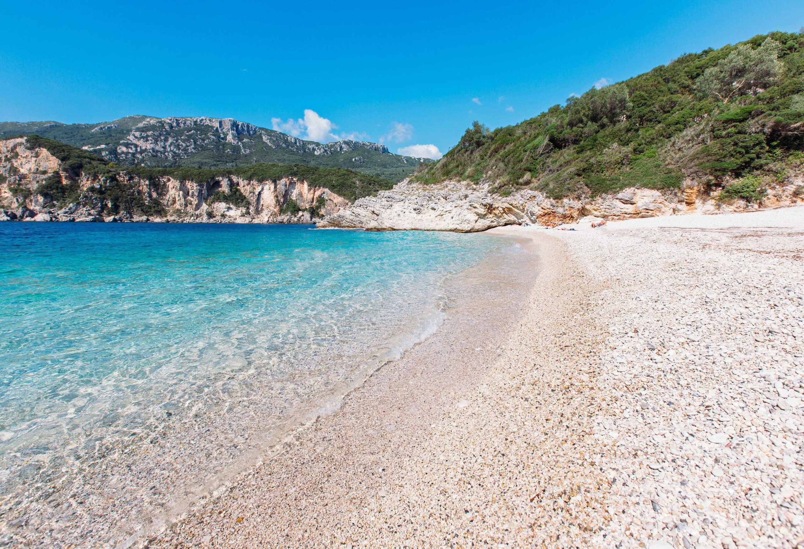 A pristine white beach with clear waters along a coast with rocky slopes.