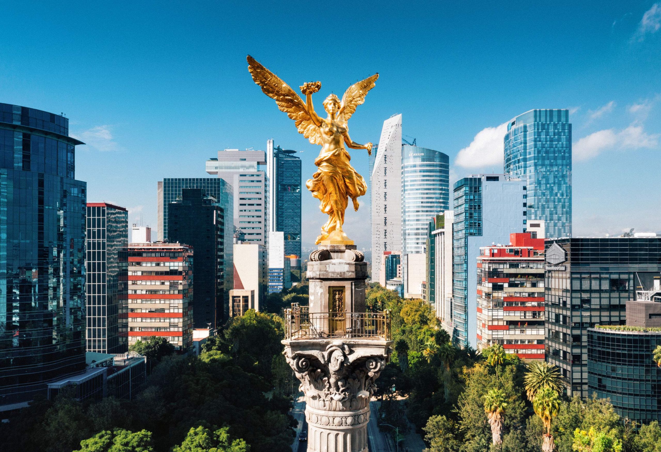A golden statue of an angel perched on a Corinthian column, surrounded by the tall structures of the city.