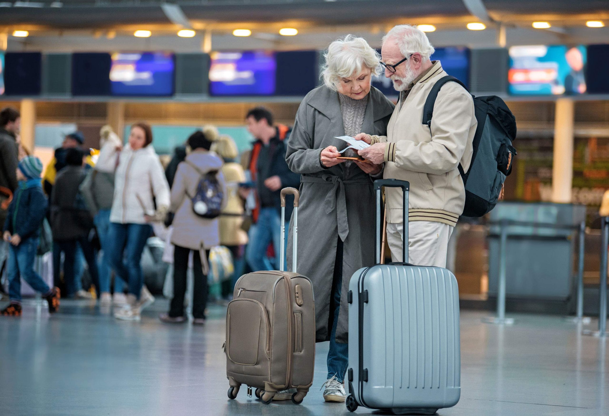 A senior couple standing with their luggage in the middle of an airport looking at their ticket.