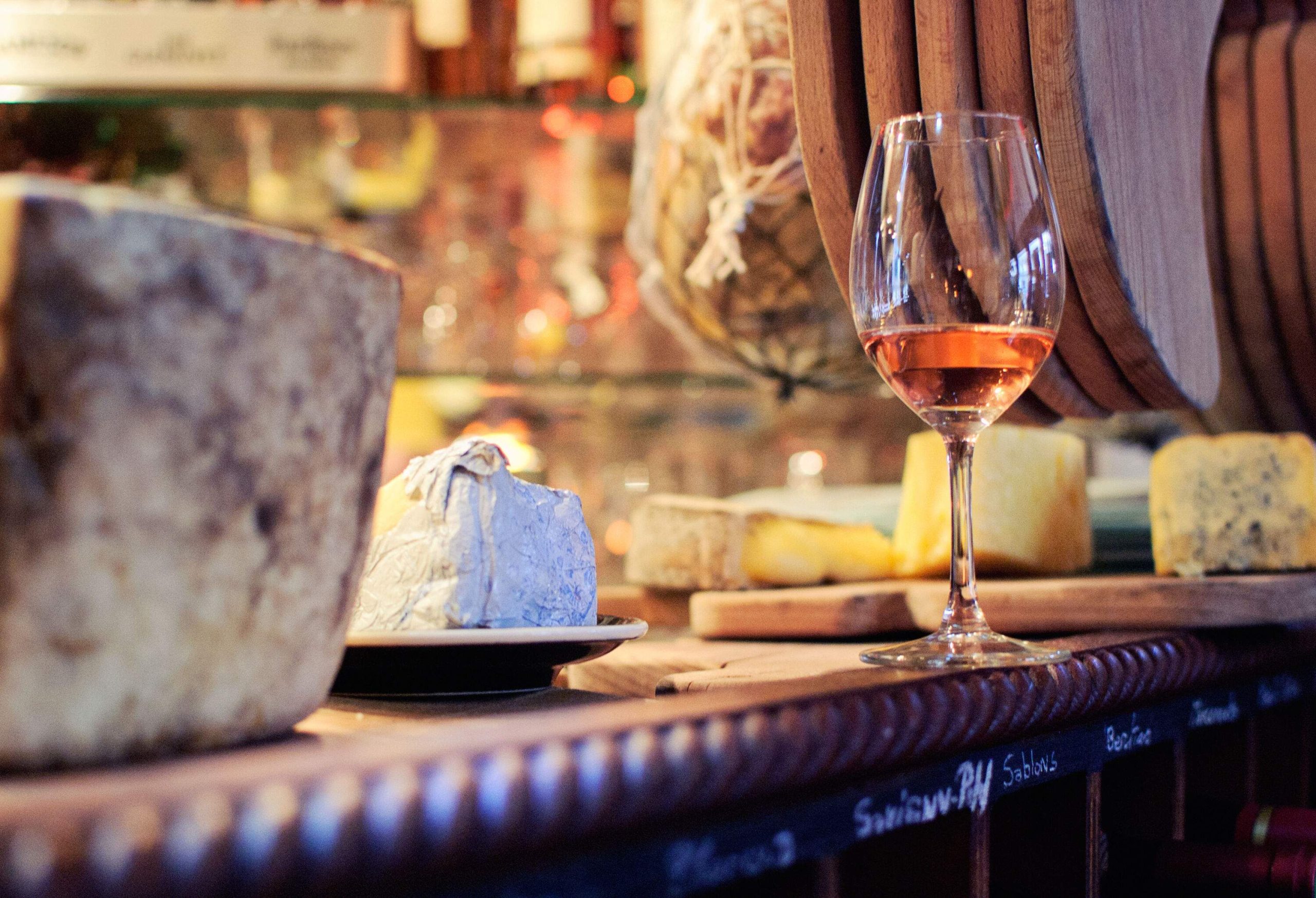 A glass of wine alongside cheese is placed on a counter bar.