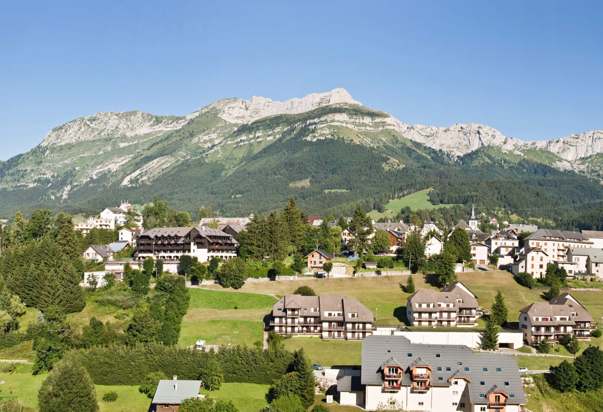 A rural region scattered with houses, trees, and grasses, backed by a mountain range.