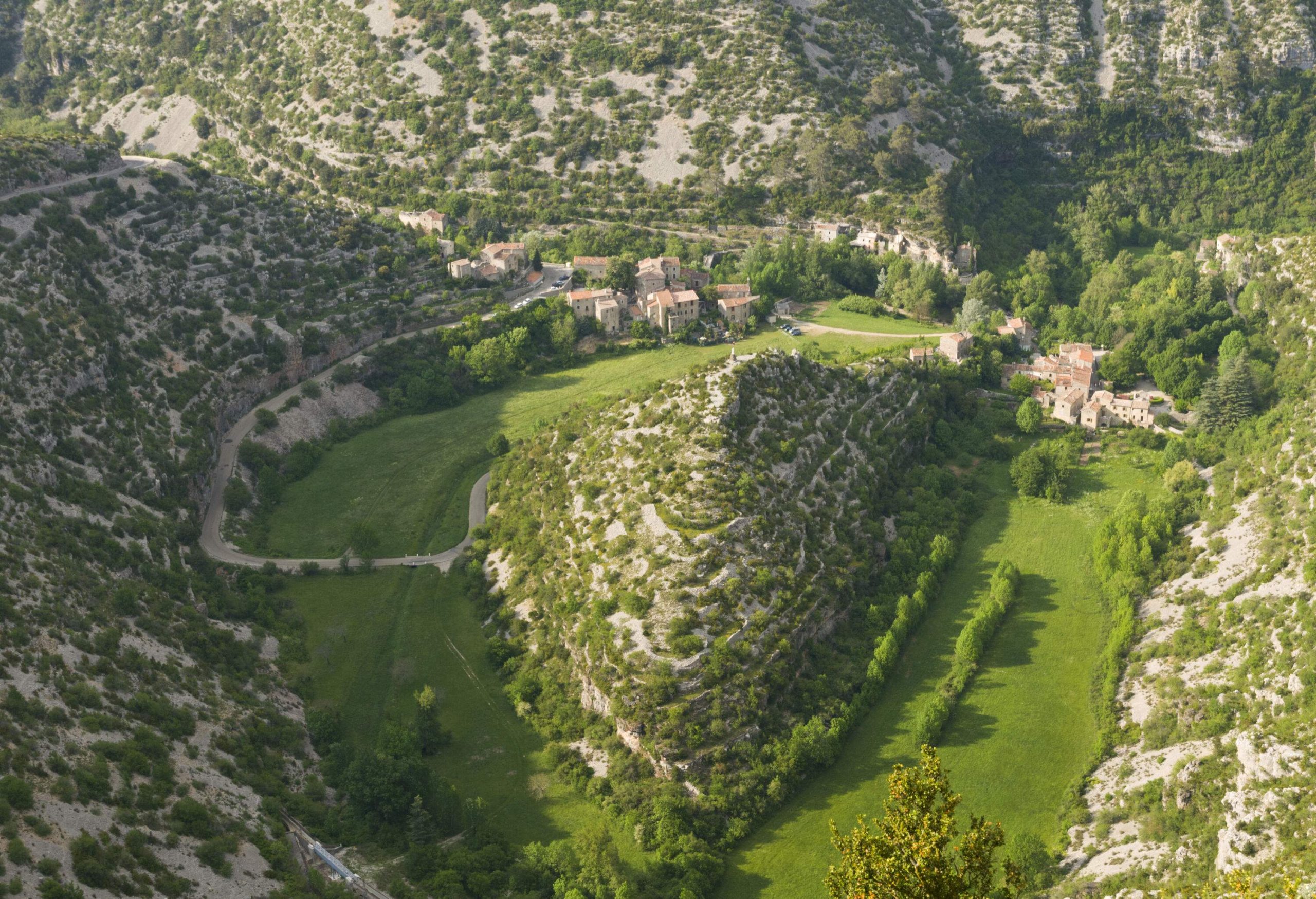 A pyramid-shaped landform surrounded by hills, trees, bushes, and a few houses.