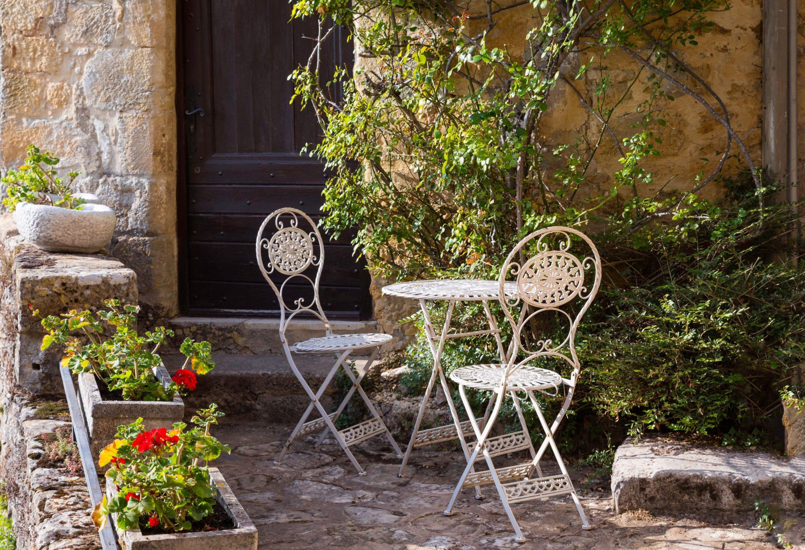a cozy patio with metal white chairs and table between the blooming flowers and plants in france