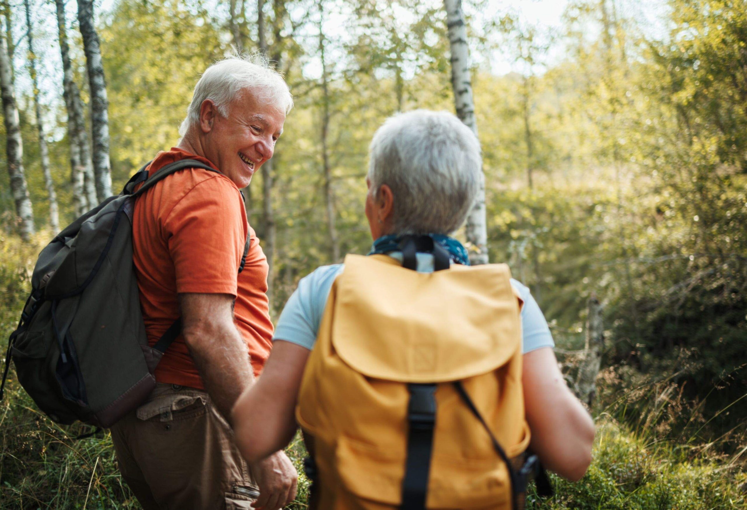 Senior hikers bonding while hiking together in forest on sunny day