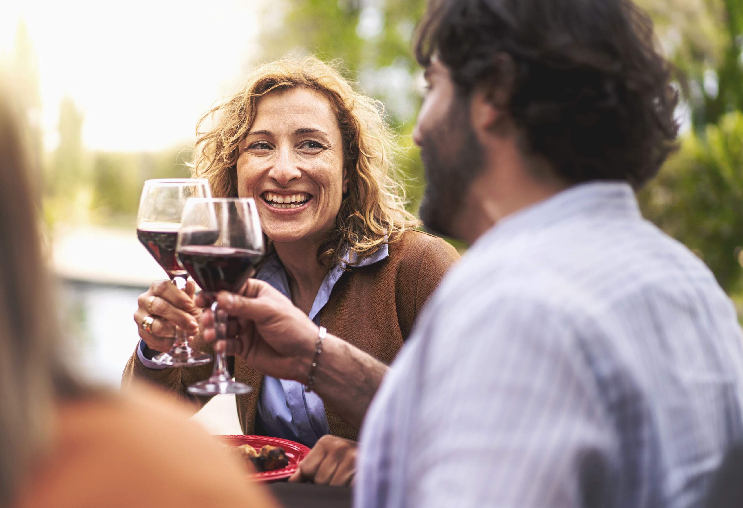 A curly blonde woman smiles with a man while making a toast with wine glasses.