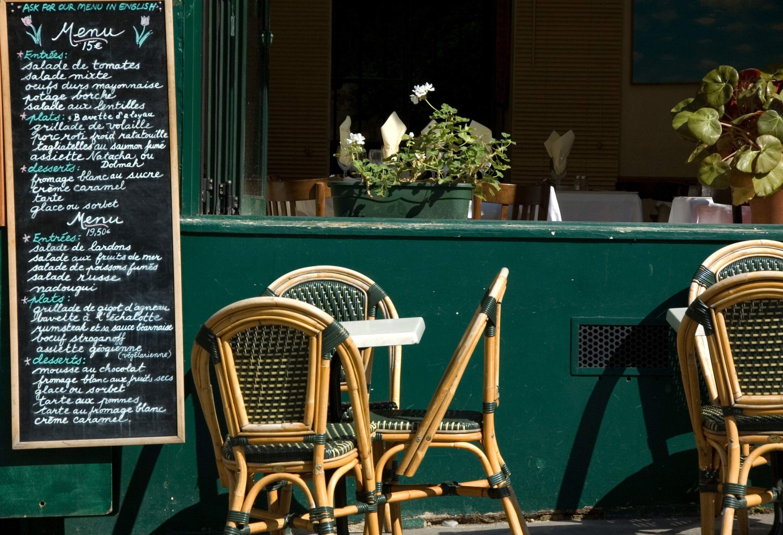 The menu of an outside restaurant is posted on a chalkboard along the sidewalk.