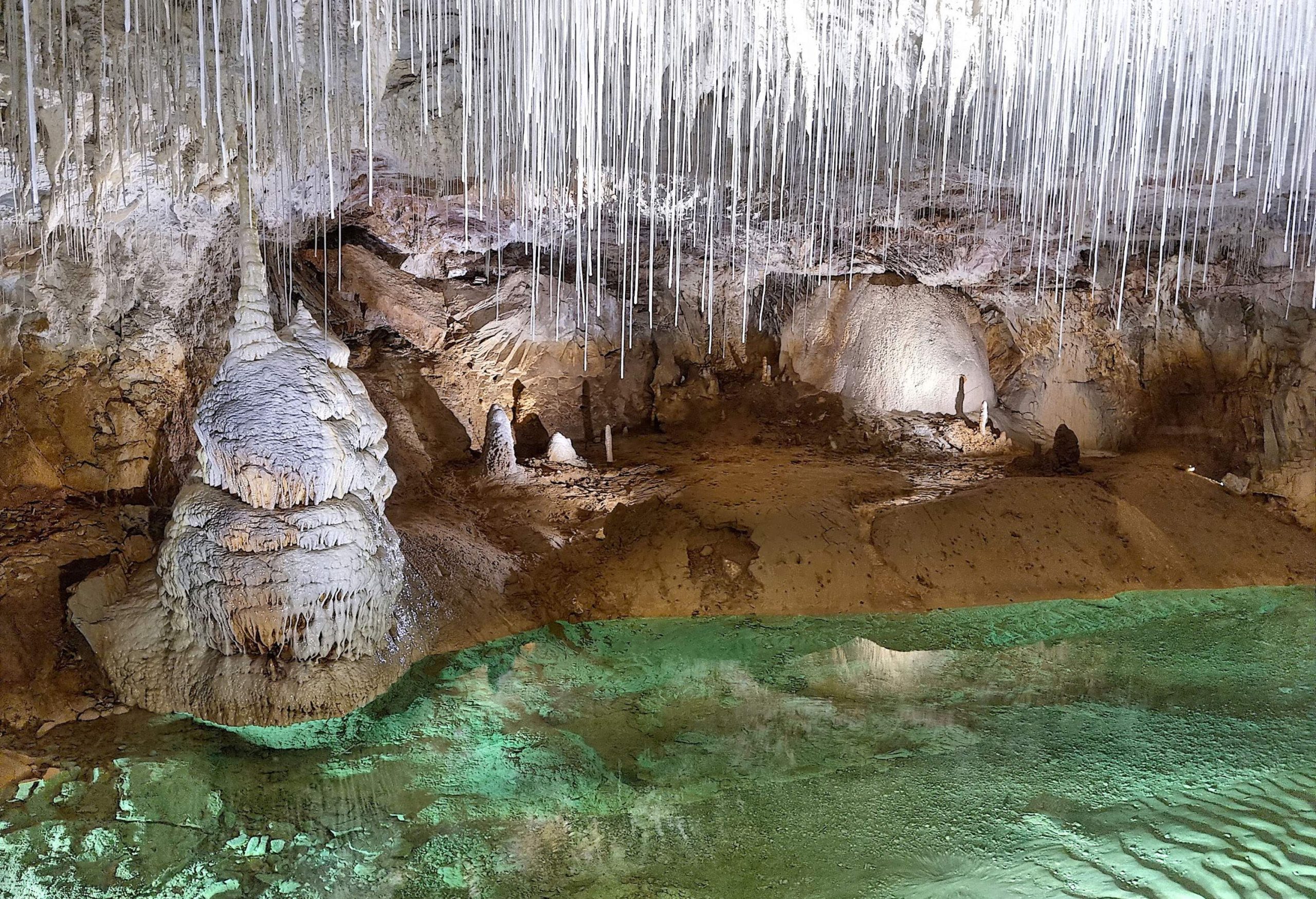 Thin spires of stalactites protruding from the ceiling of a cave with a rippling sandy floor.