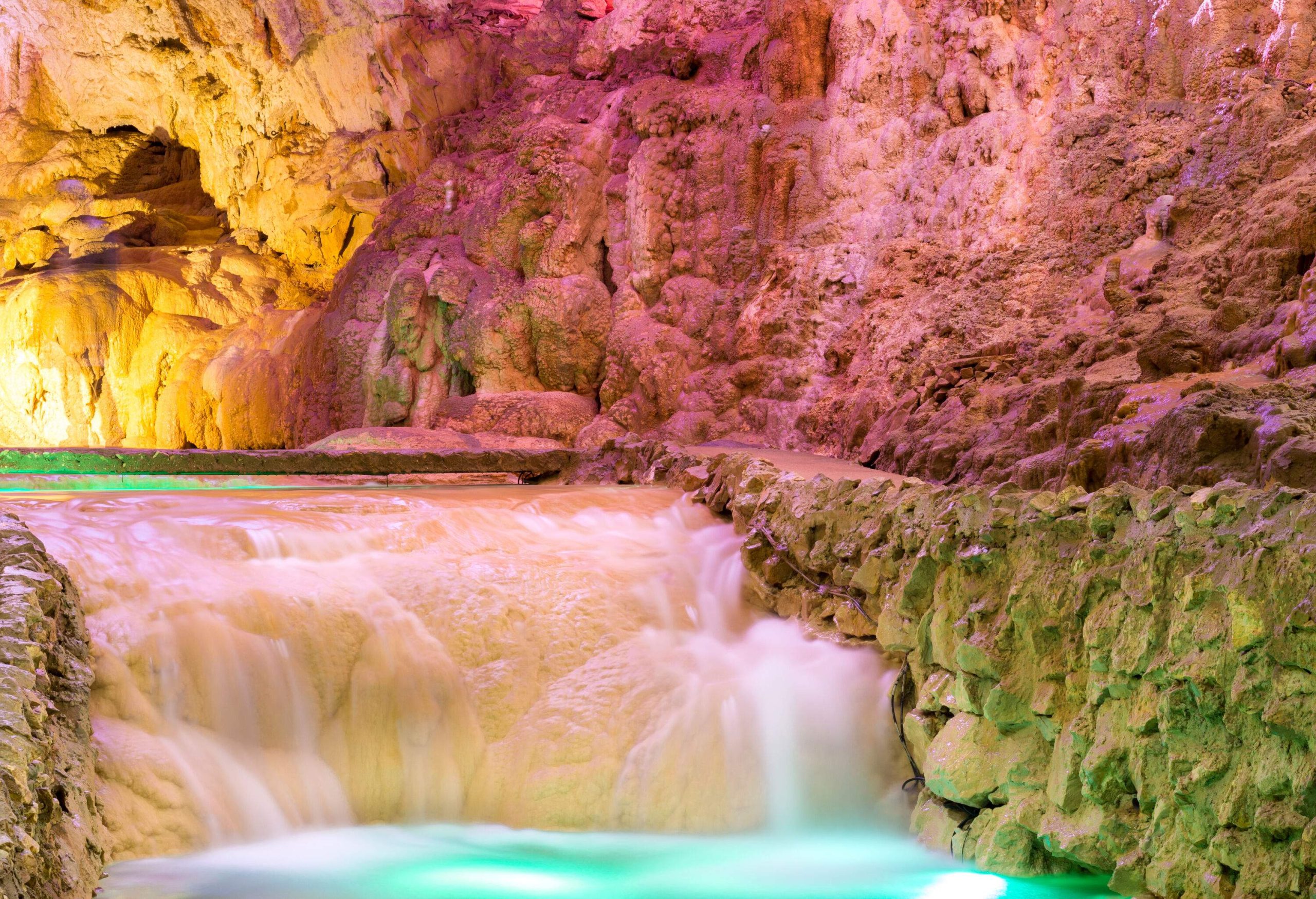 Water flows into a small stream surrounded by walls of vibrant rock formations.