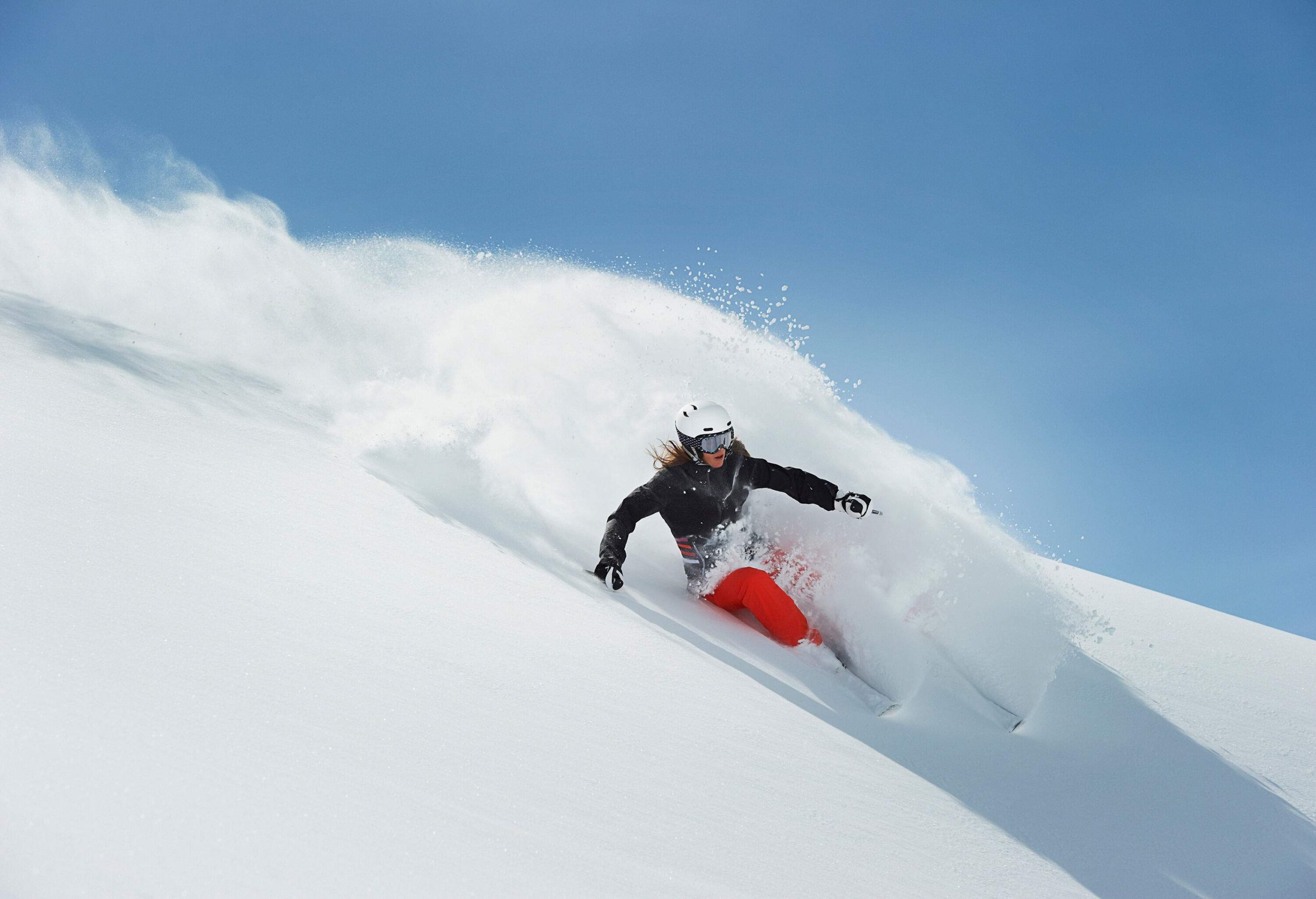 Woman side-slipping on a steep slope with a trail of snow splash.