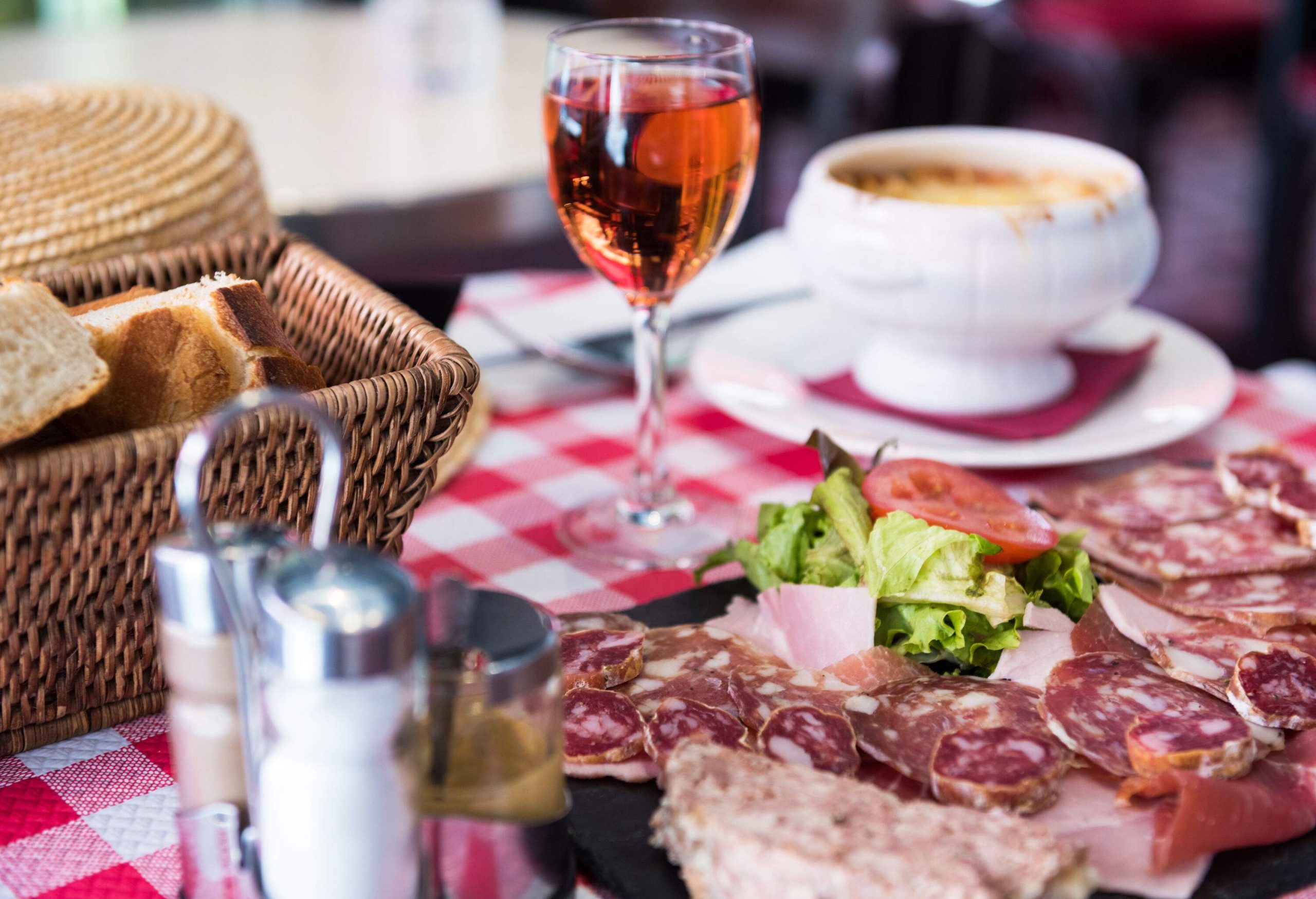 On a table covered with a checkered cloth were placed cured meat, wine in a glass, bread, and soup.