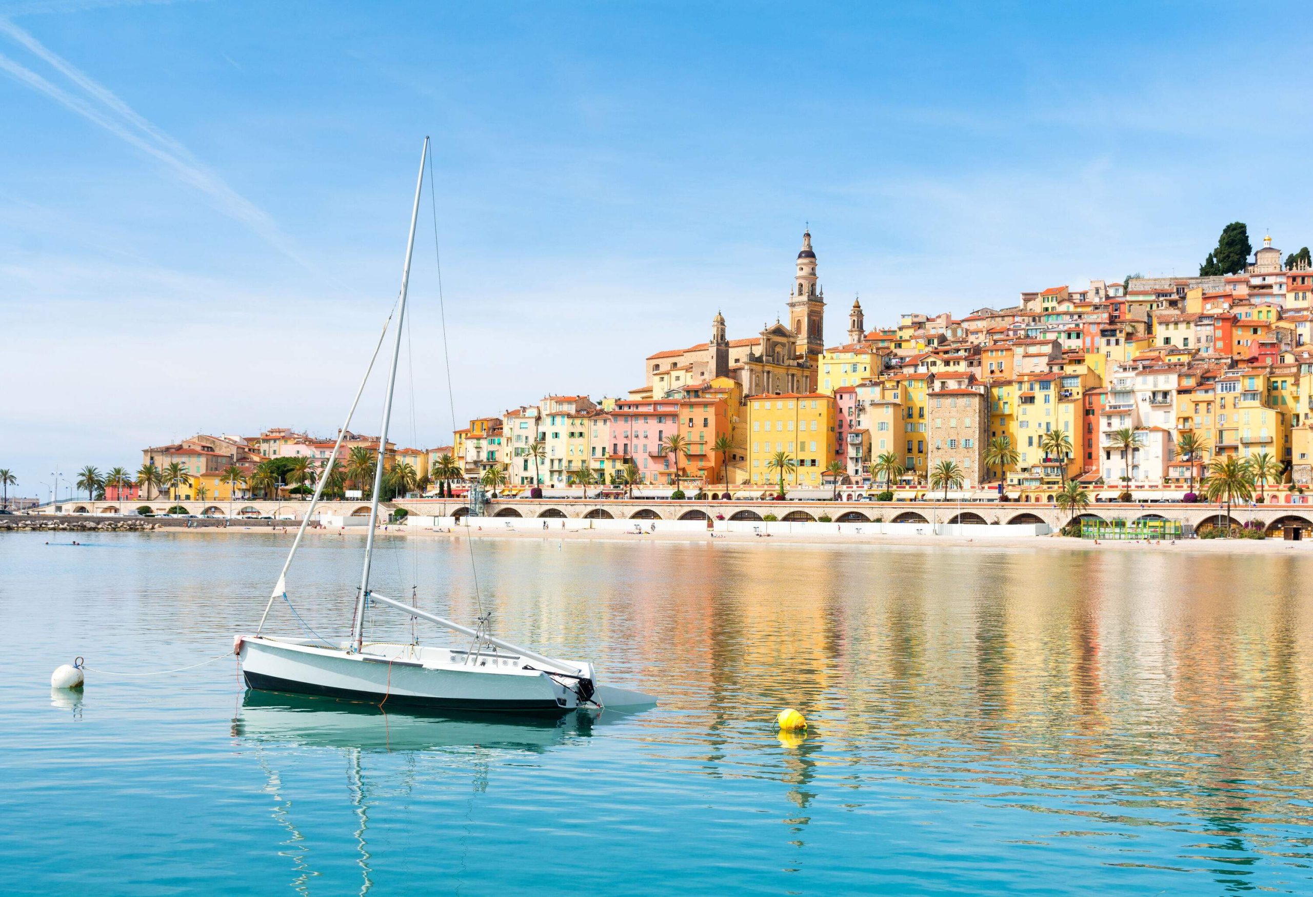 A small boat in the ocean overlooking the colourful coastal cityscape with classic buildings against the cloudy blue sky.