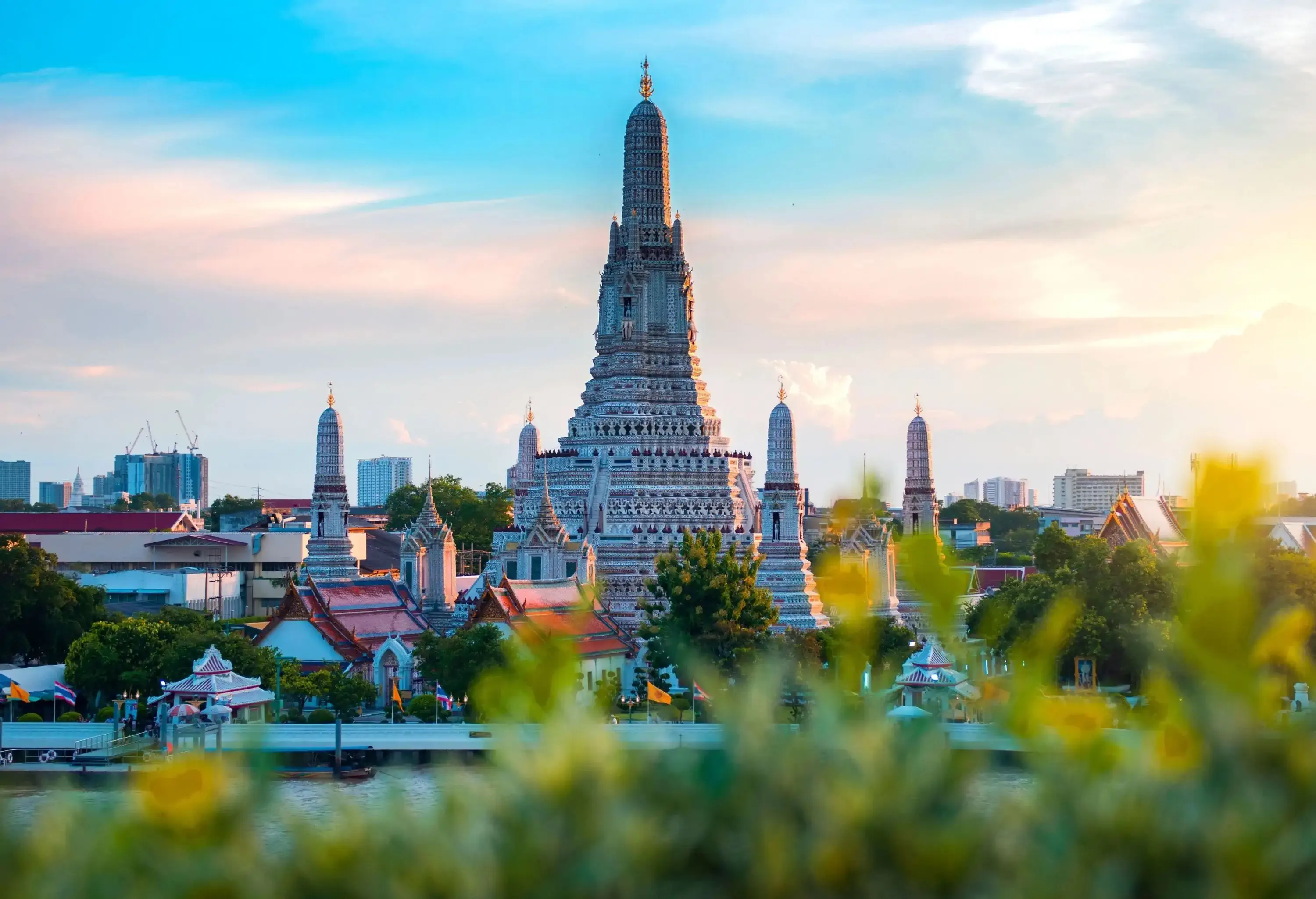 The elaborately carved central spire of Wat Arun rising above the smaller towers and other structures nearby.
