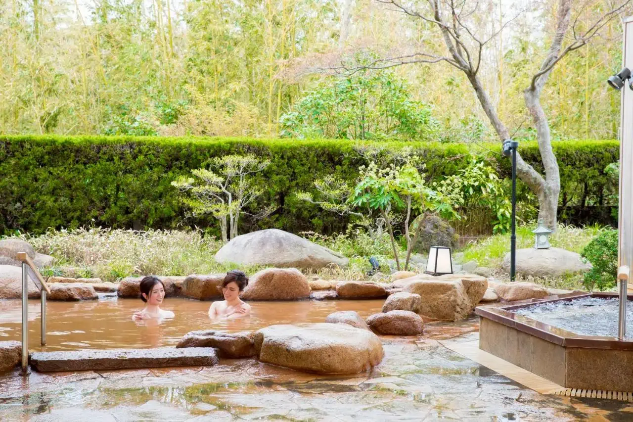 Two women bathing in a Japanese onsen surrounded by greenery