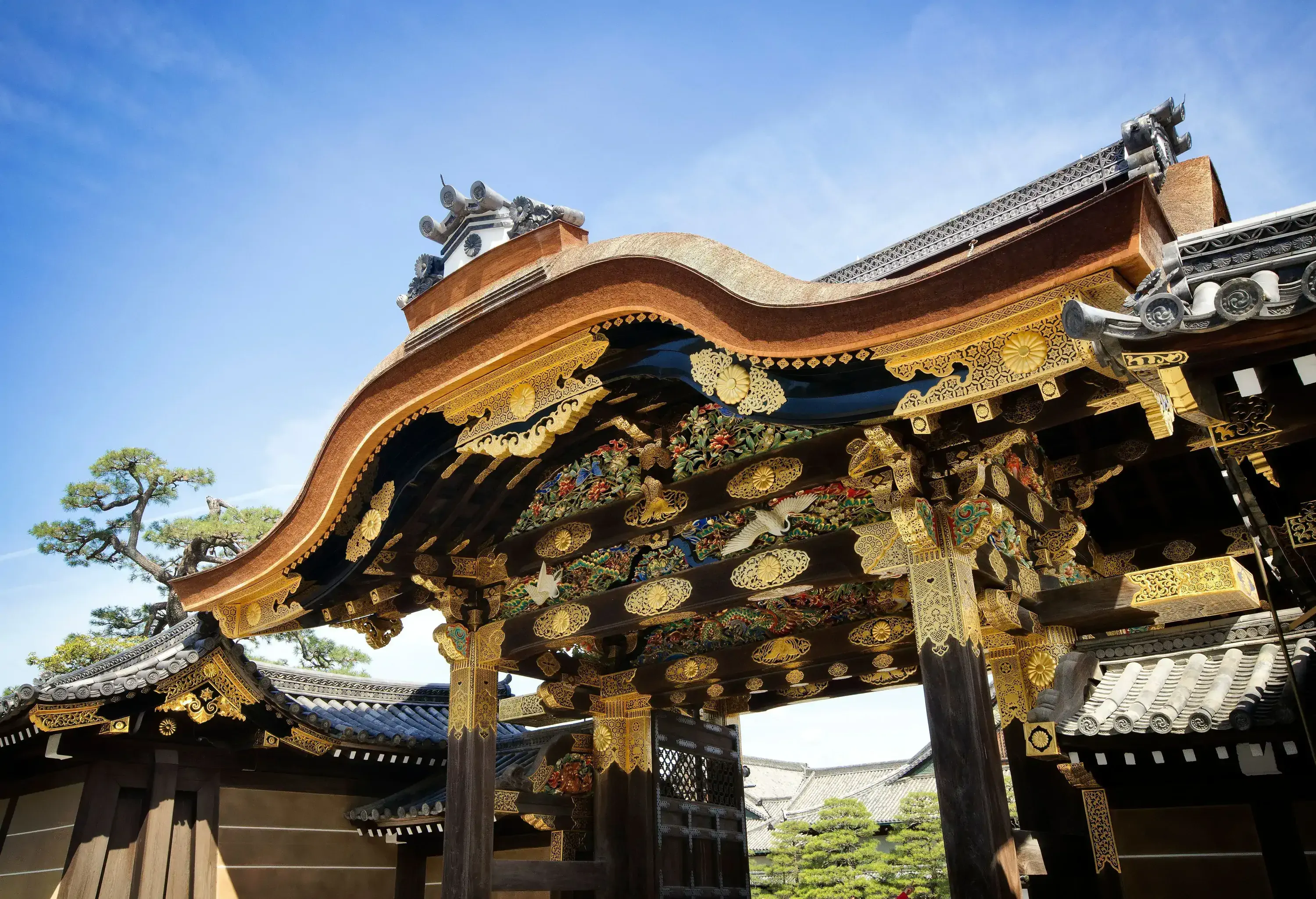 A castle gate with intricate golden carvings of cranes, pines, bamboos, and flower blossoms.
