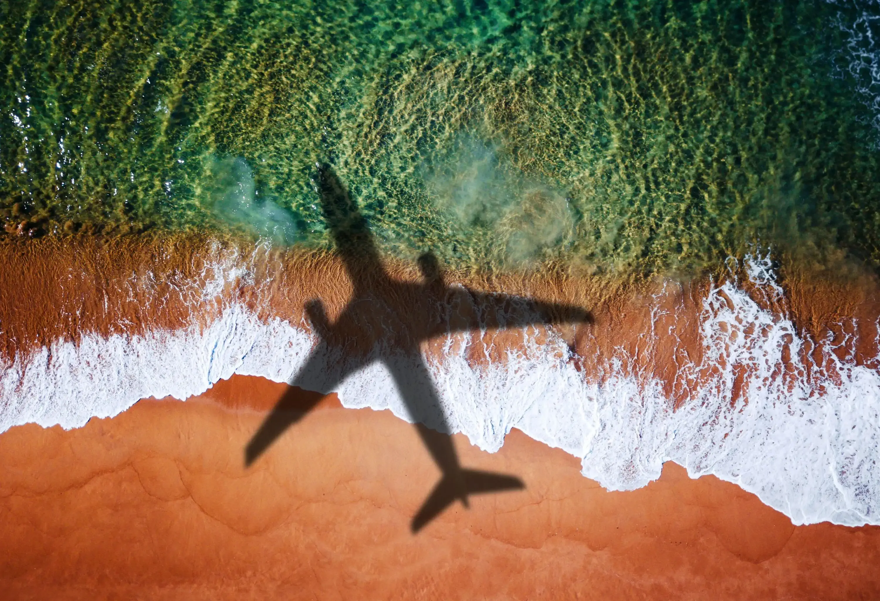 A shadow of an airplane gracefully gliding over a pristine beach with crystal-clear water.