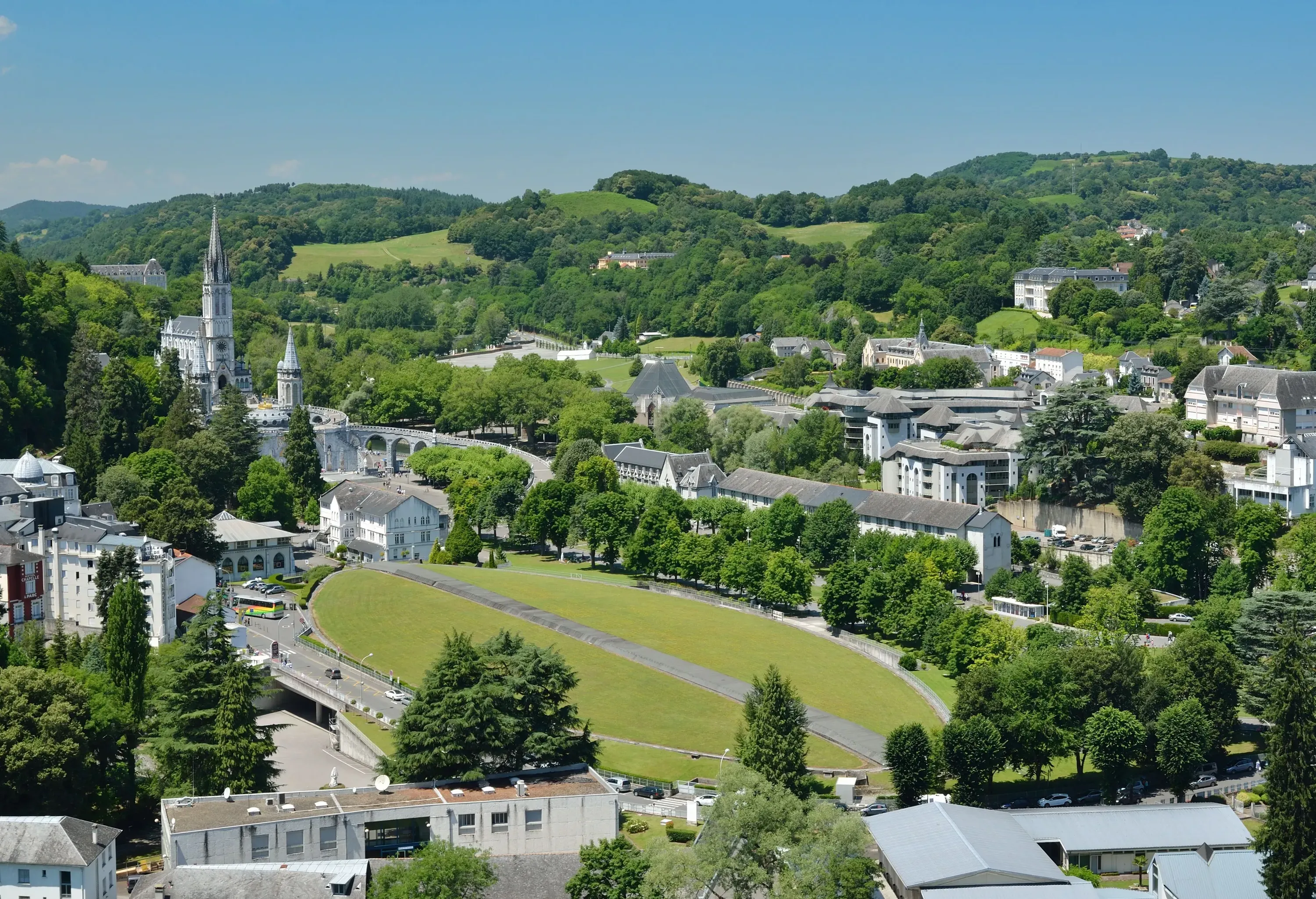 A massive oval green lawn surrounded by trees and town buildings.