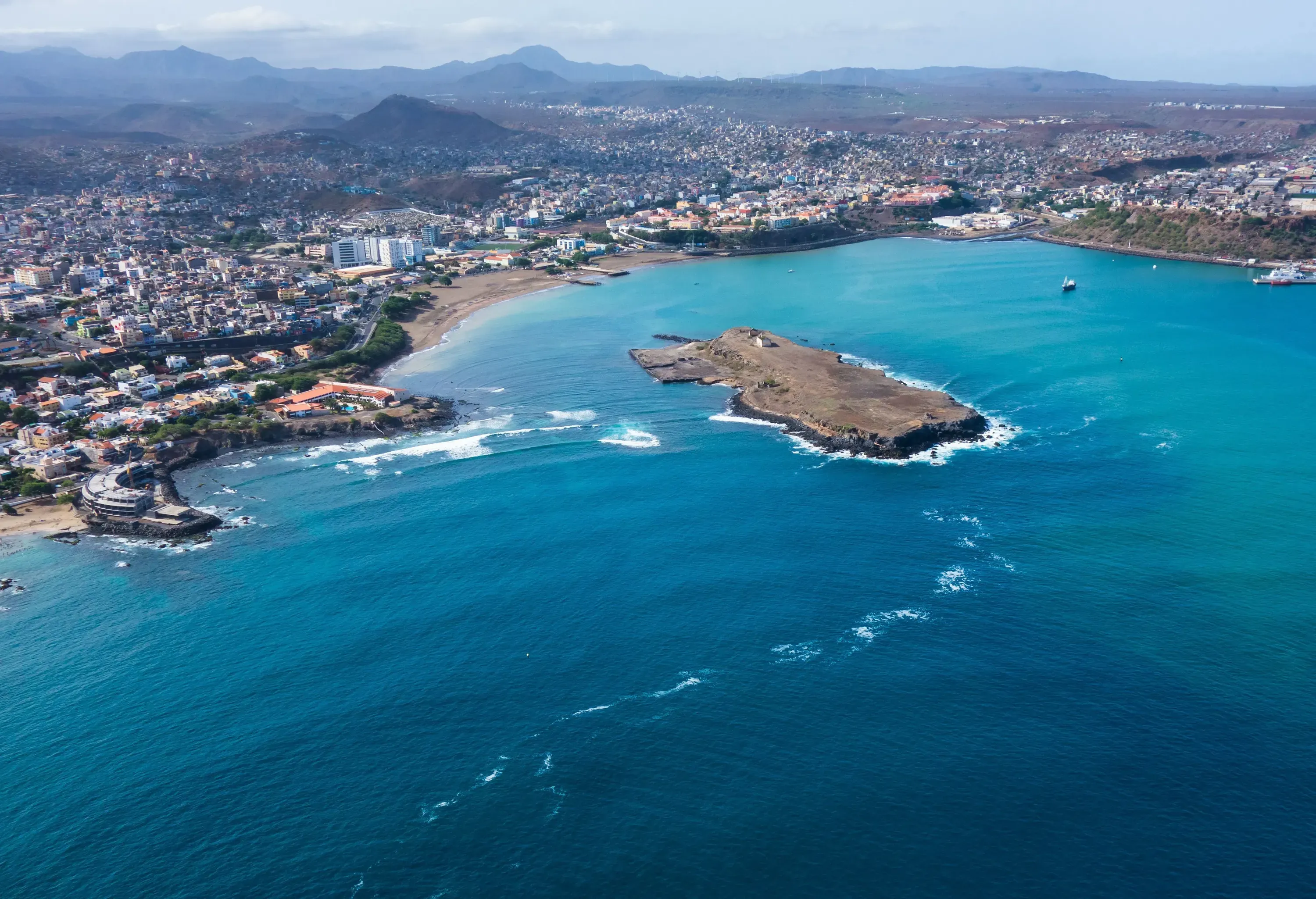 A coastal city nestled around a scenic bay area, featuring a captivating rock formation island at its centre.
