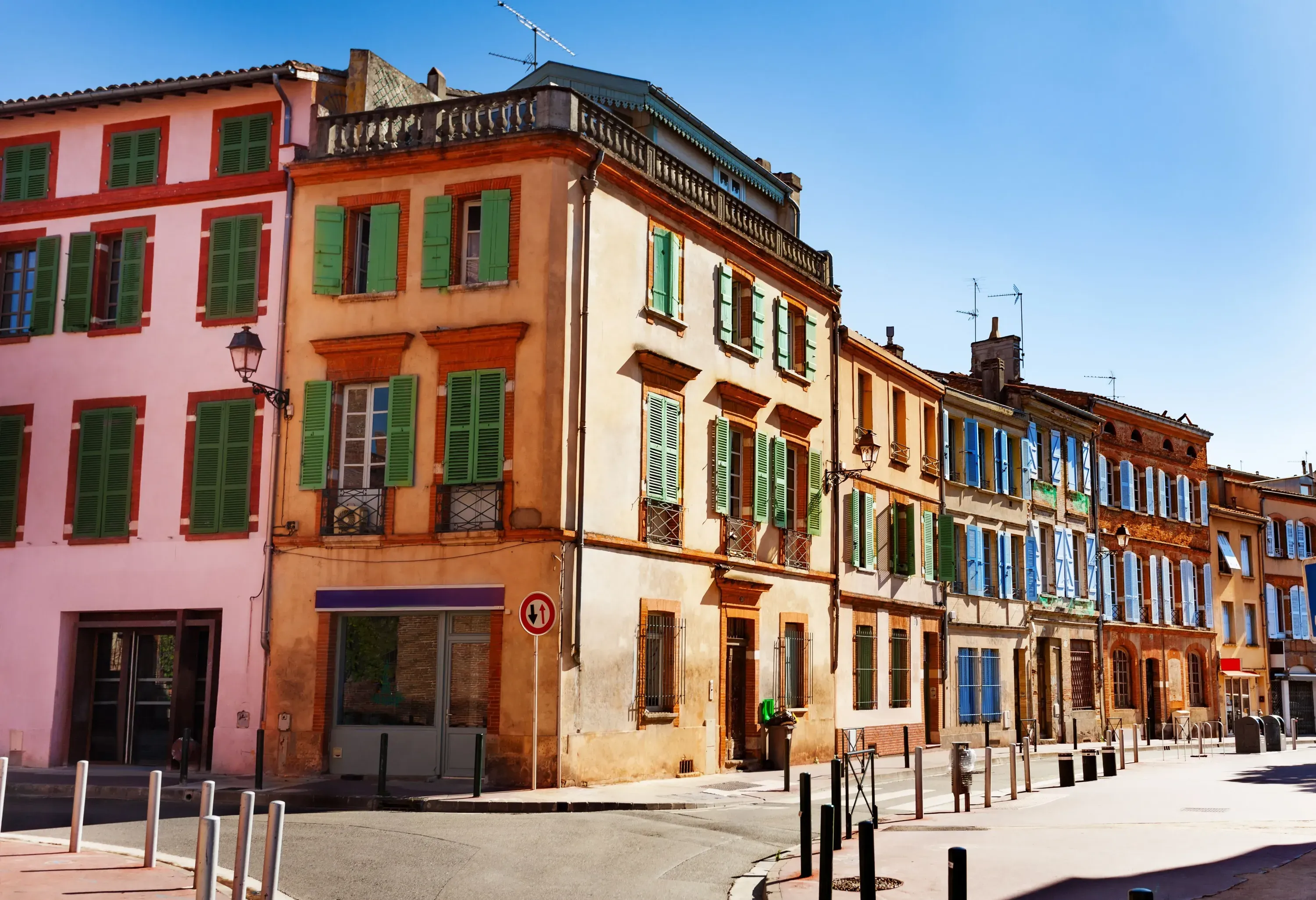 Colourful residential buildings lined up alongside a narrow asphalt street on a sunny day.