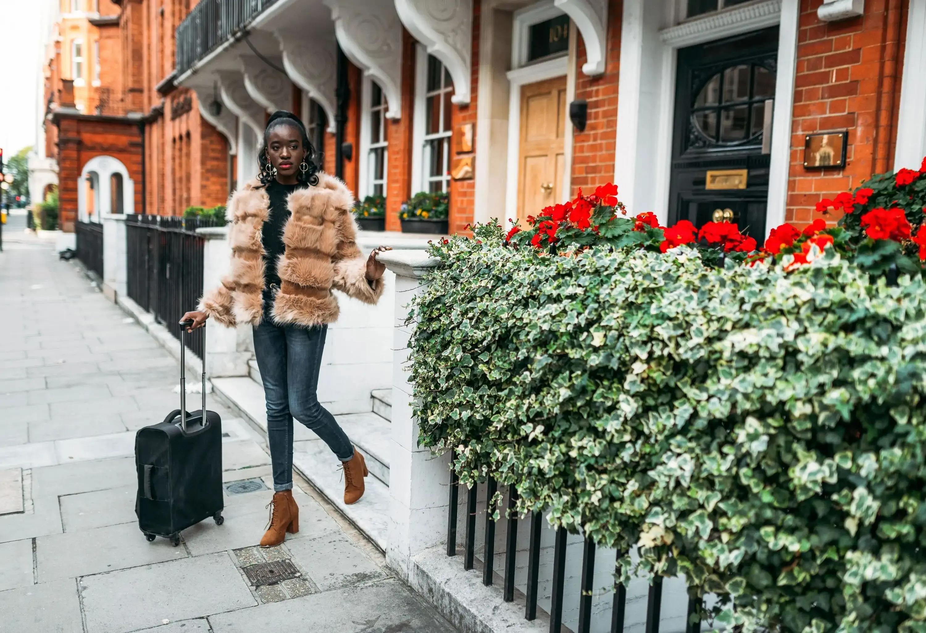 A dark-skinned lady traveller with a suitcase at the doorstep leaving the guesthouse.