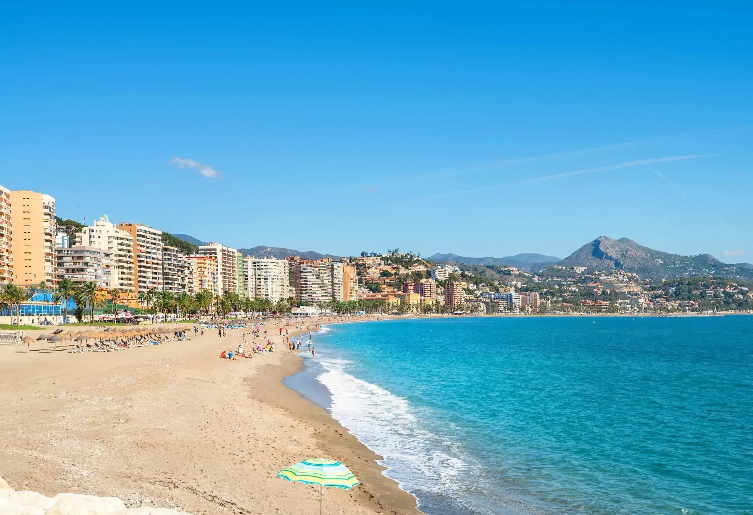 A crowded beach with views of high-rise buildings along the coast.