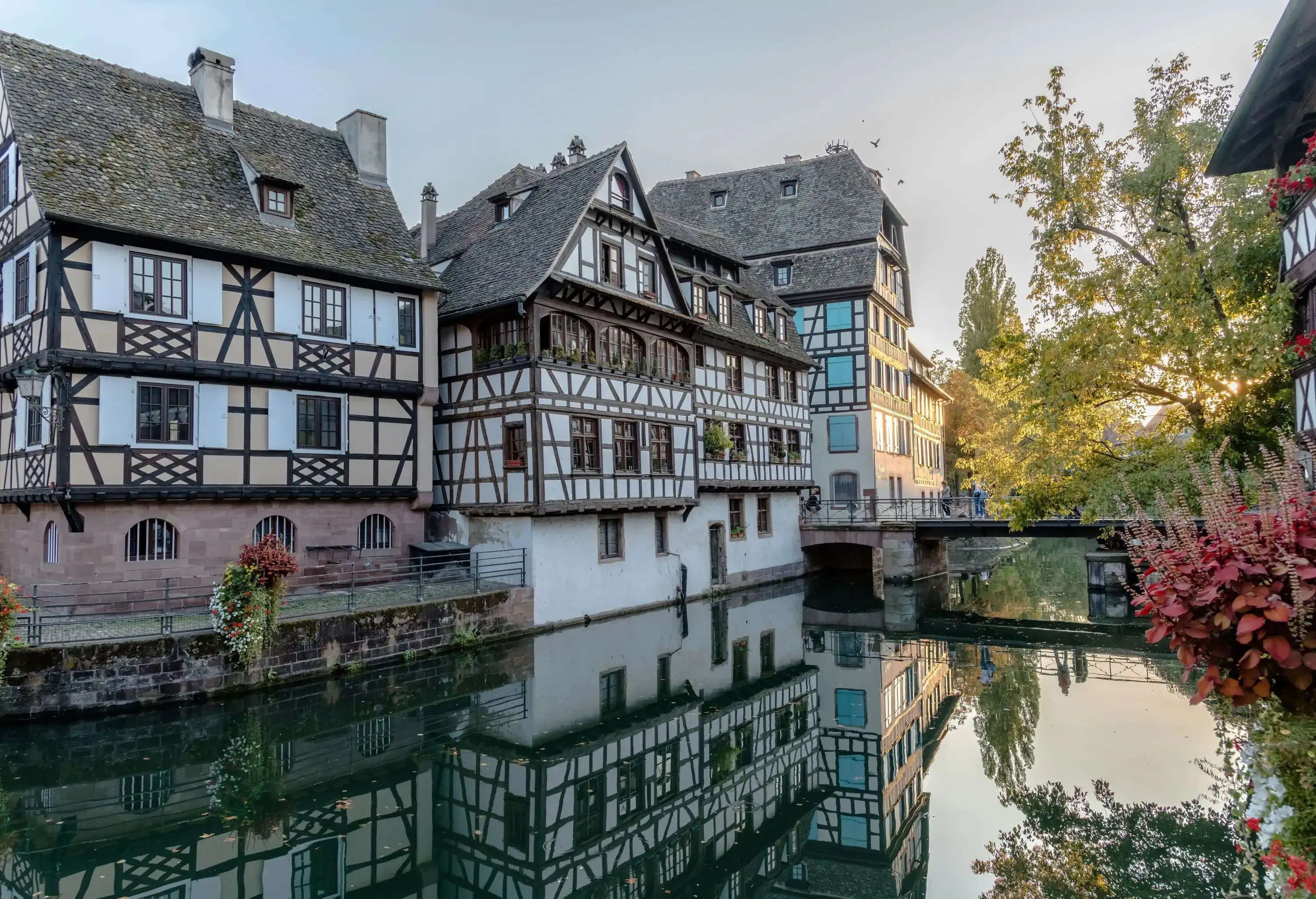 A row of half-timbered buildings nestled alongside a canal with a pathway bridge.