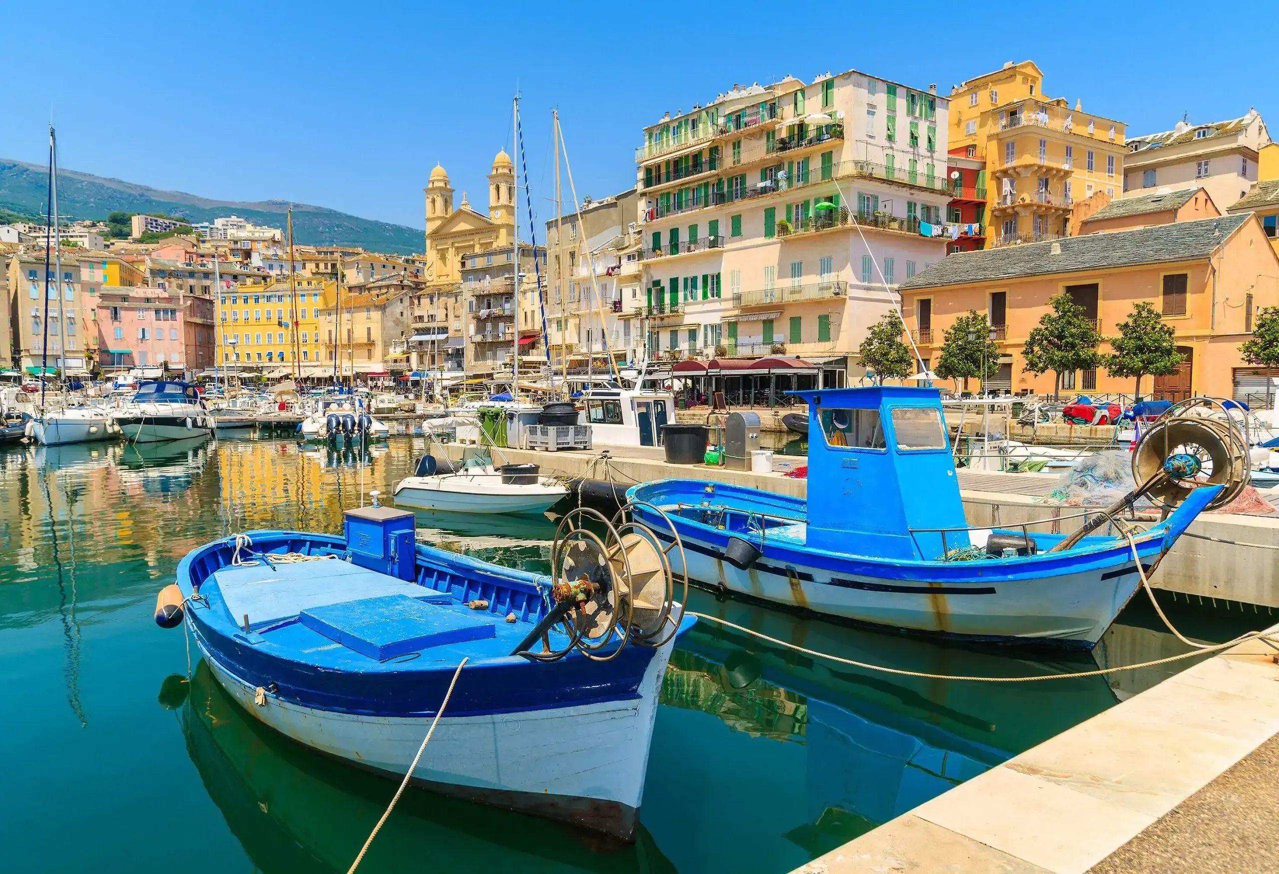 Fishing boats moored in a harbour across from the colourful buildings along the coast.