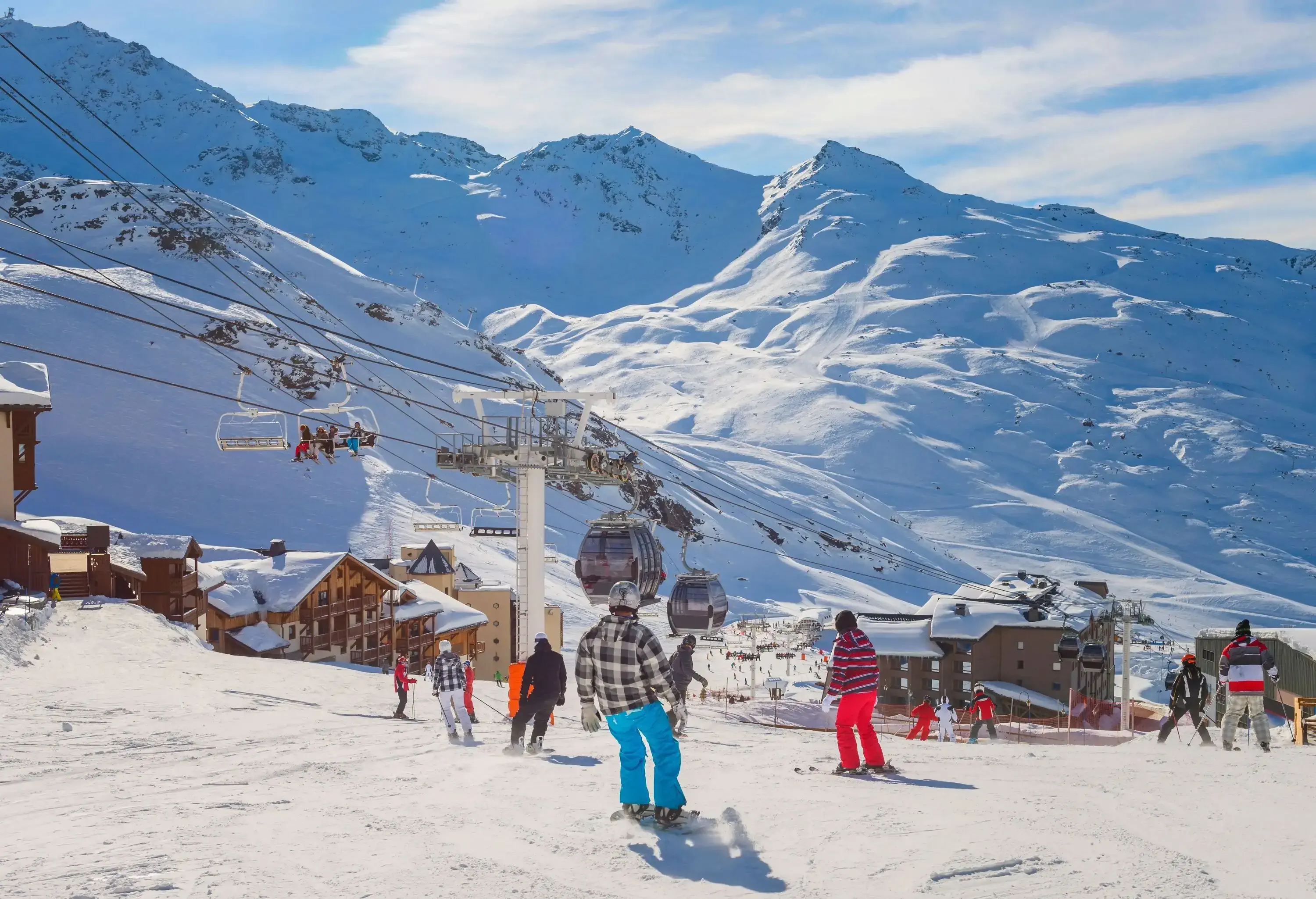 Crowd of skiers descending a snow hill with views of hanging chairlifts and cable cars above a ski village.