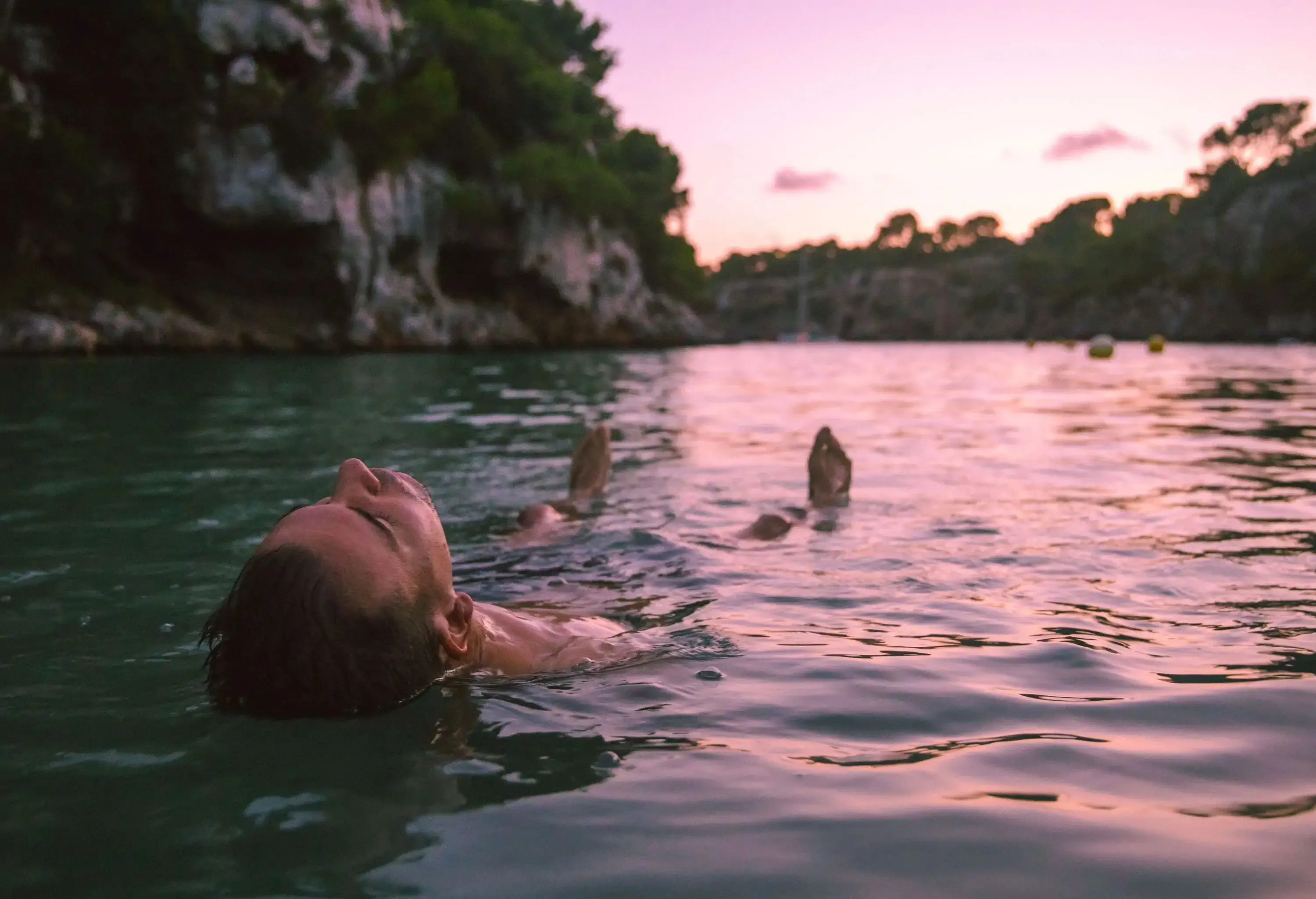 A person relaxing as he floats on the seawater beneath the lush cliffs.
