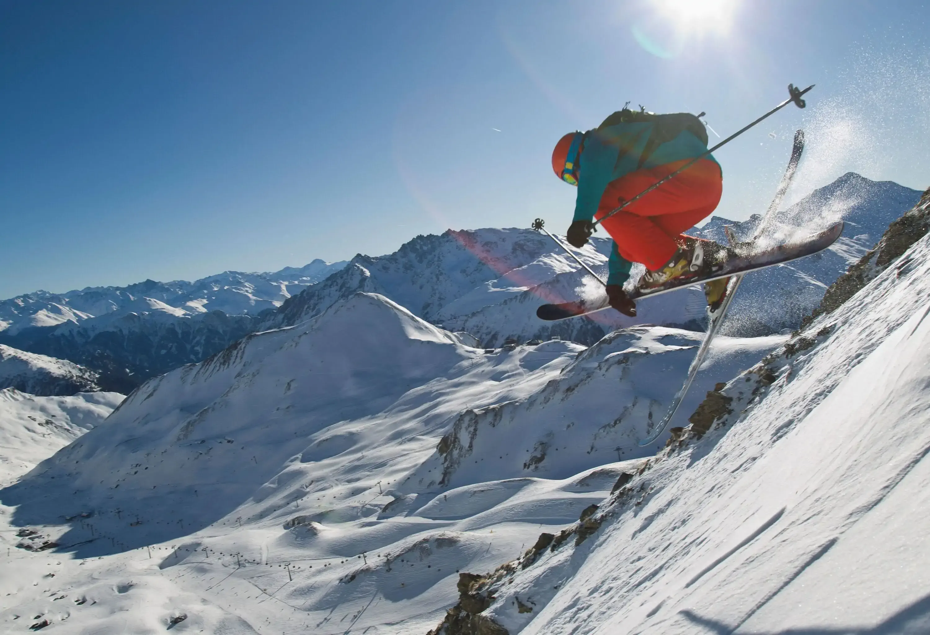 An skier jumping off as he descends a snowy hill.