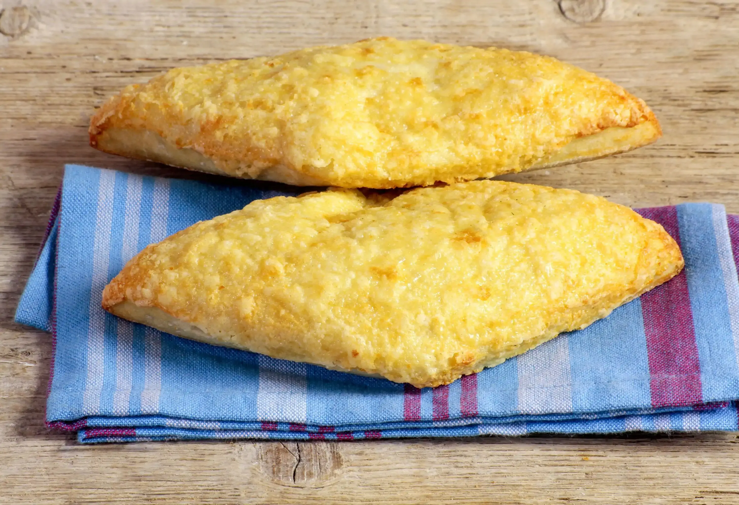 Two bread rolls with cheese crusts set on a tea towel.