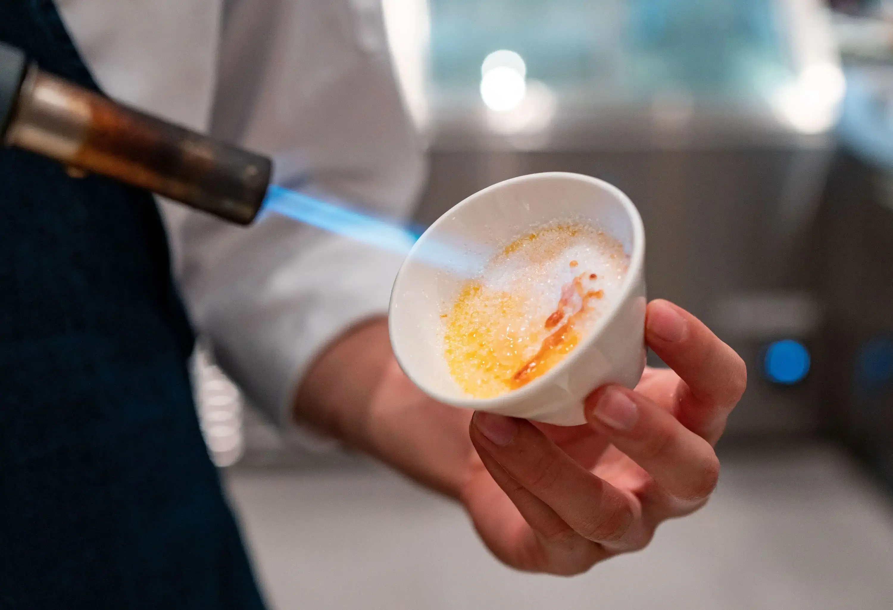 An individual holds a torch to burn the sugar on creme brulee desert.