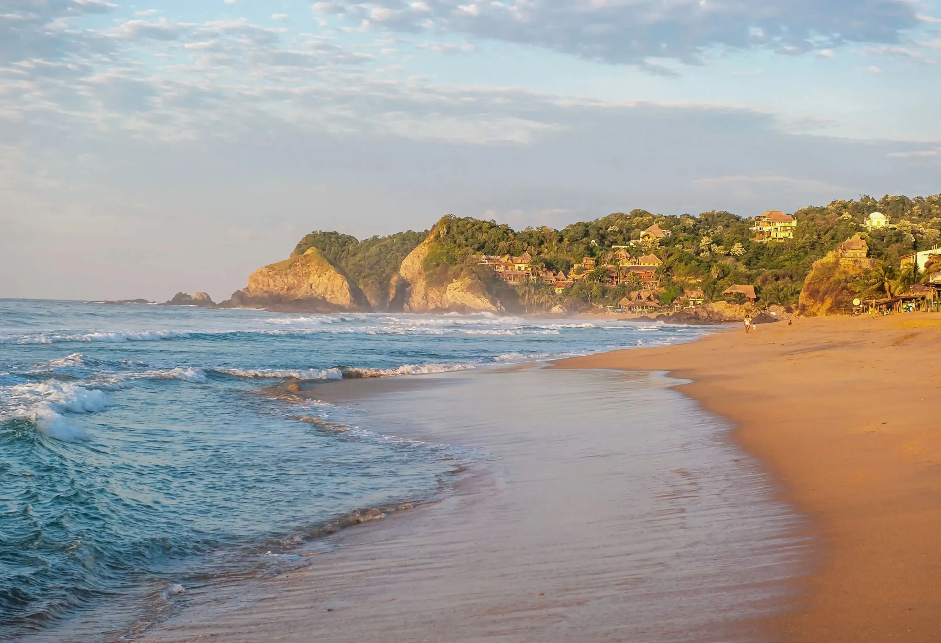 A golden sand beach with hillside houses in the early morning mellow light.