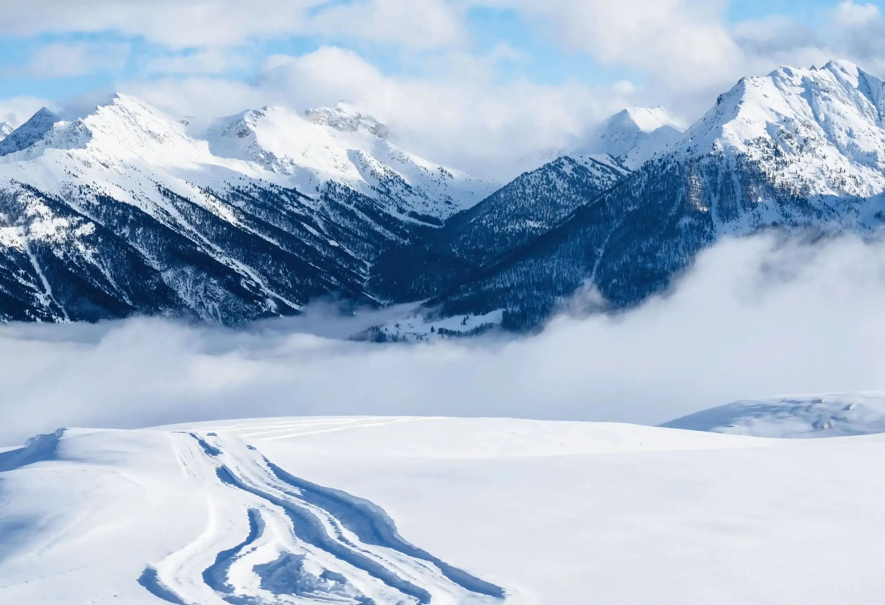 Ski tracks on a snowfield with views of snow-capped mountains covered in fog.