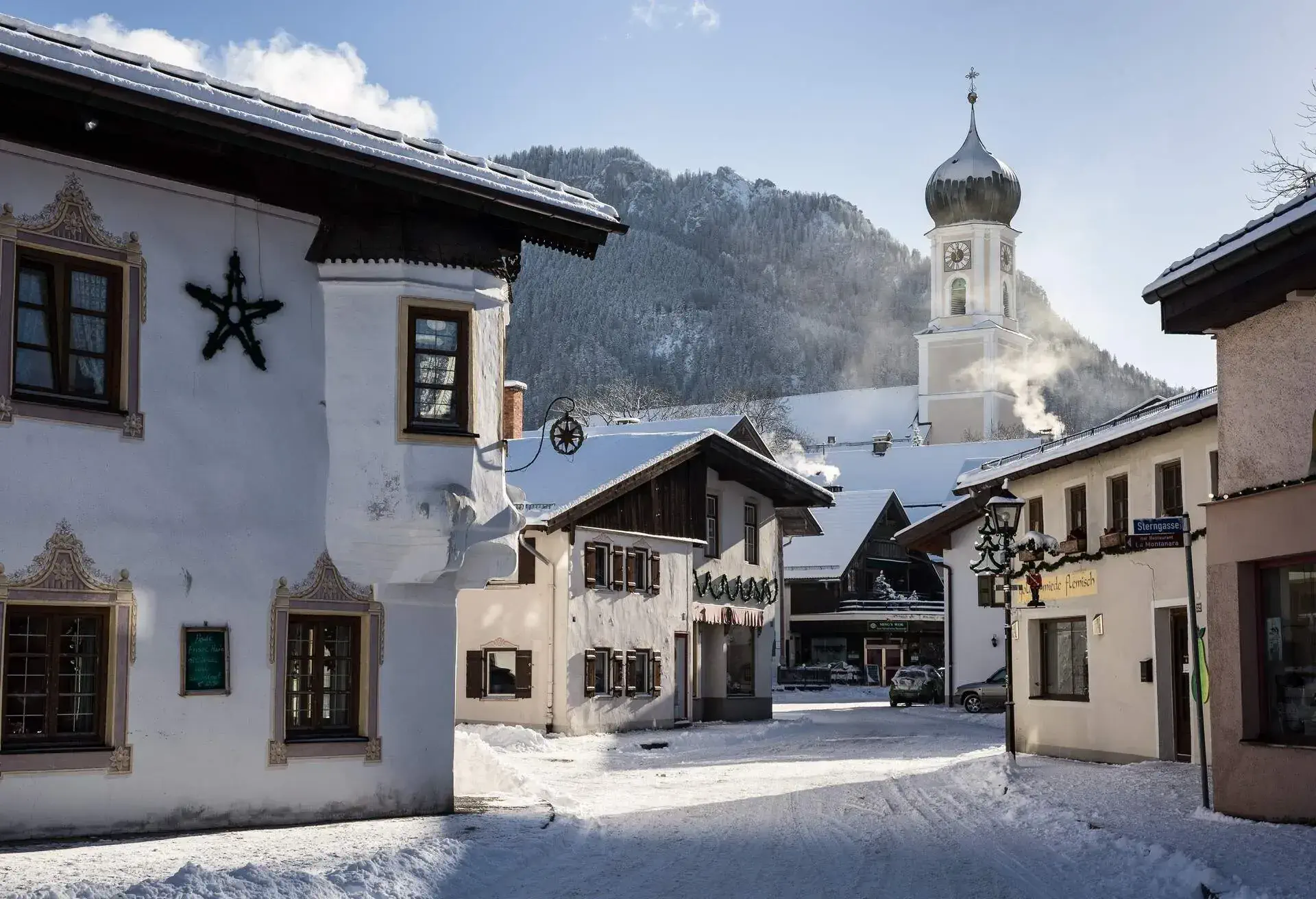 A typical street in an upper Bavarian village with traditional mural art and christmas decorations. Snow is laying on the ground and the chimneys are smoking. Oberammergau, Bavaria, Germany.