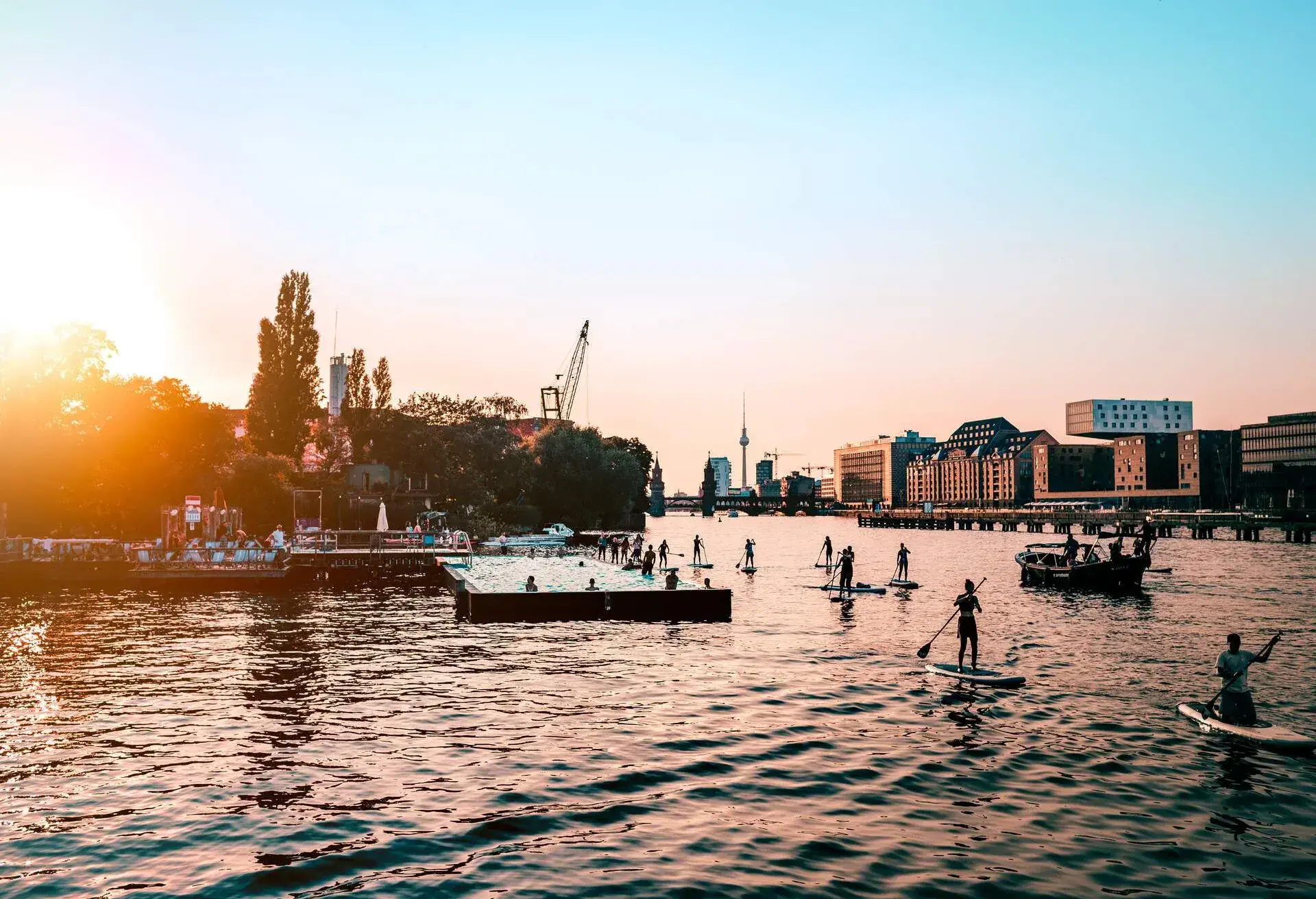 People paddleboarding across a river at sunset.