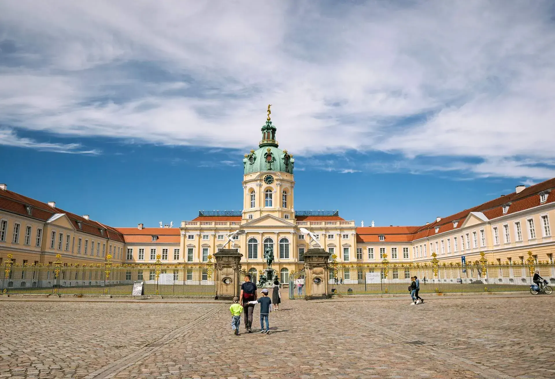 People walk towards the baroque architectural palace of the symmetrical Schloss Charlottenburg in Berlin, Germany.