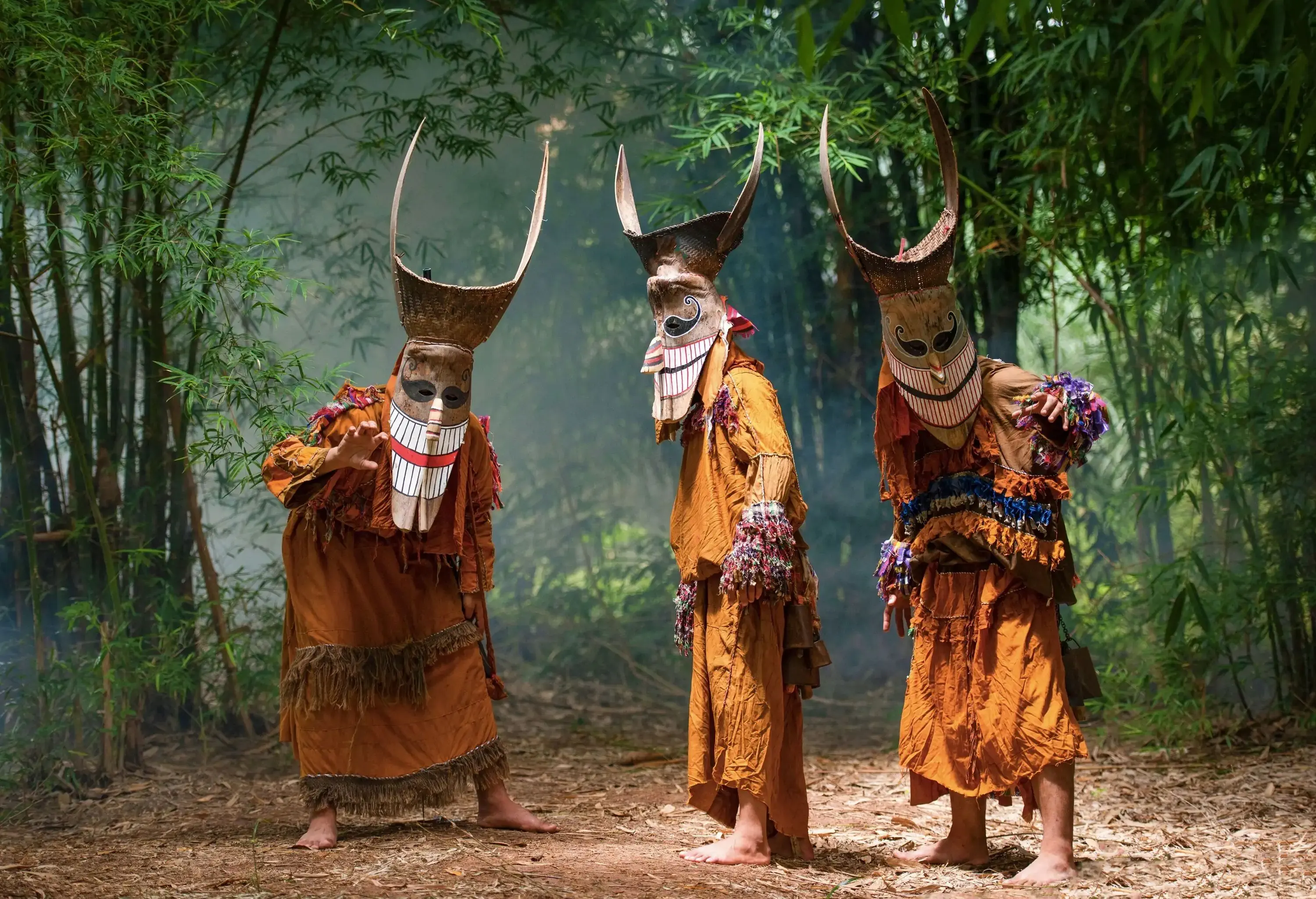Three people in colourful costumes and horned masks in a forest.