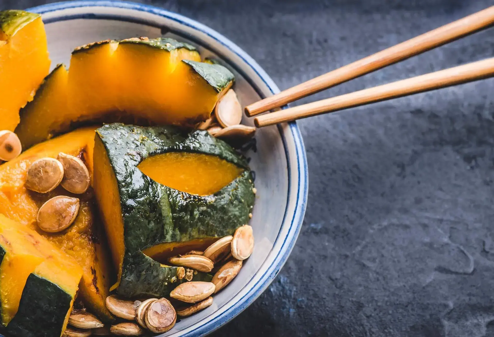 Delicious Kabocha Squash (Japanese Pumpkin) recipe. Japanese Simmered Kabocha cooked in savory dashi broth seasoned with soy sauce and sake with pumpkin seeds, close up, dark background. Web banner