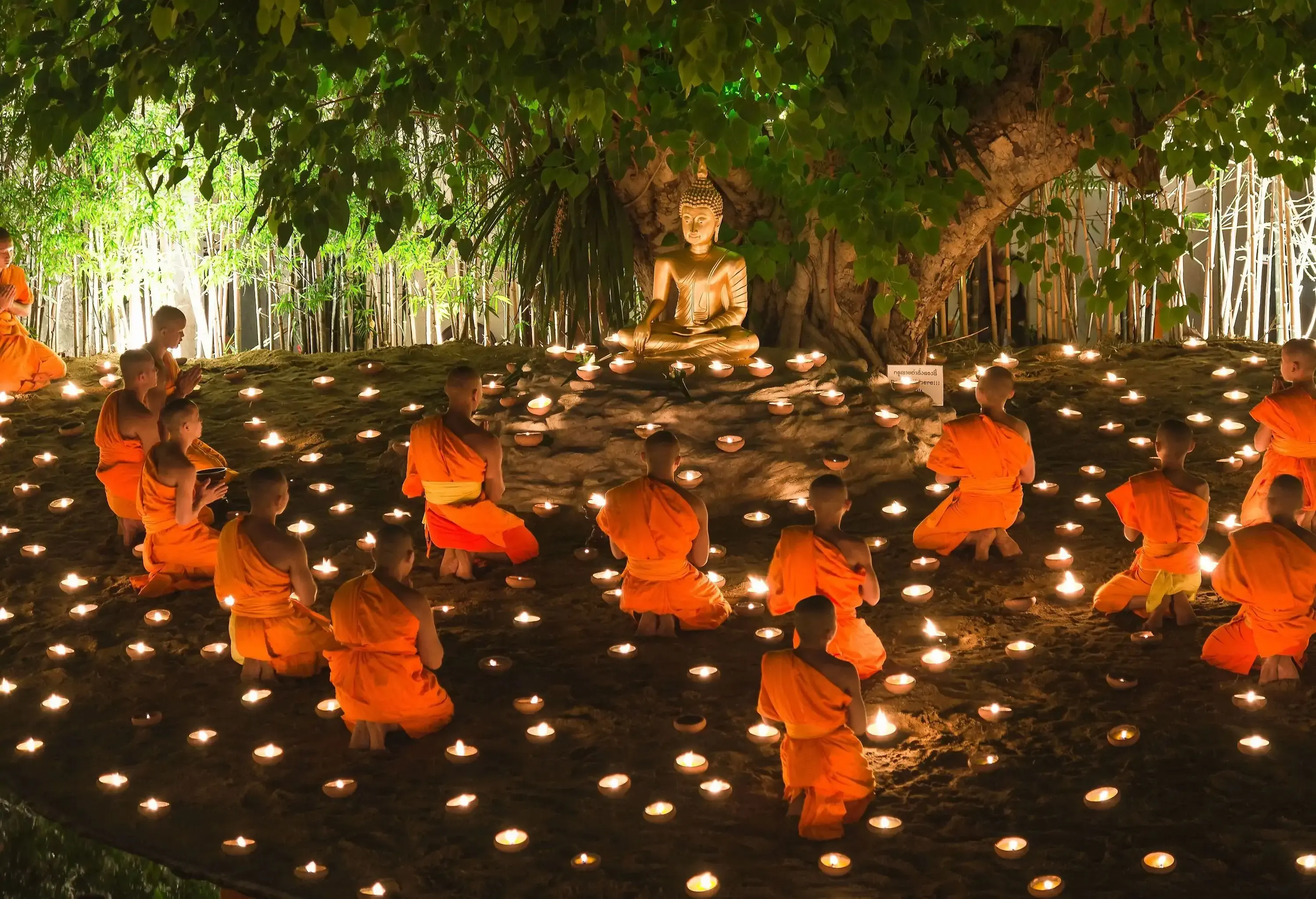 Monks and lighted candles surround the golden Buddha under the Bo tree.