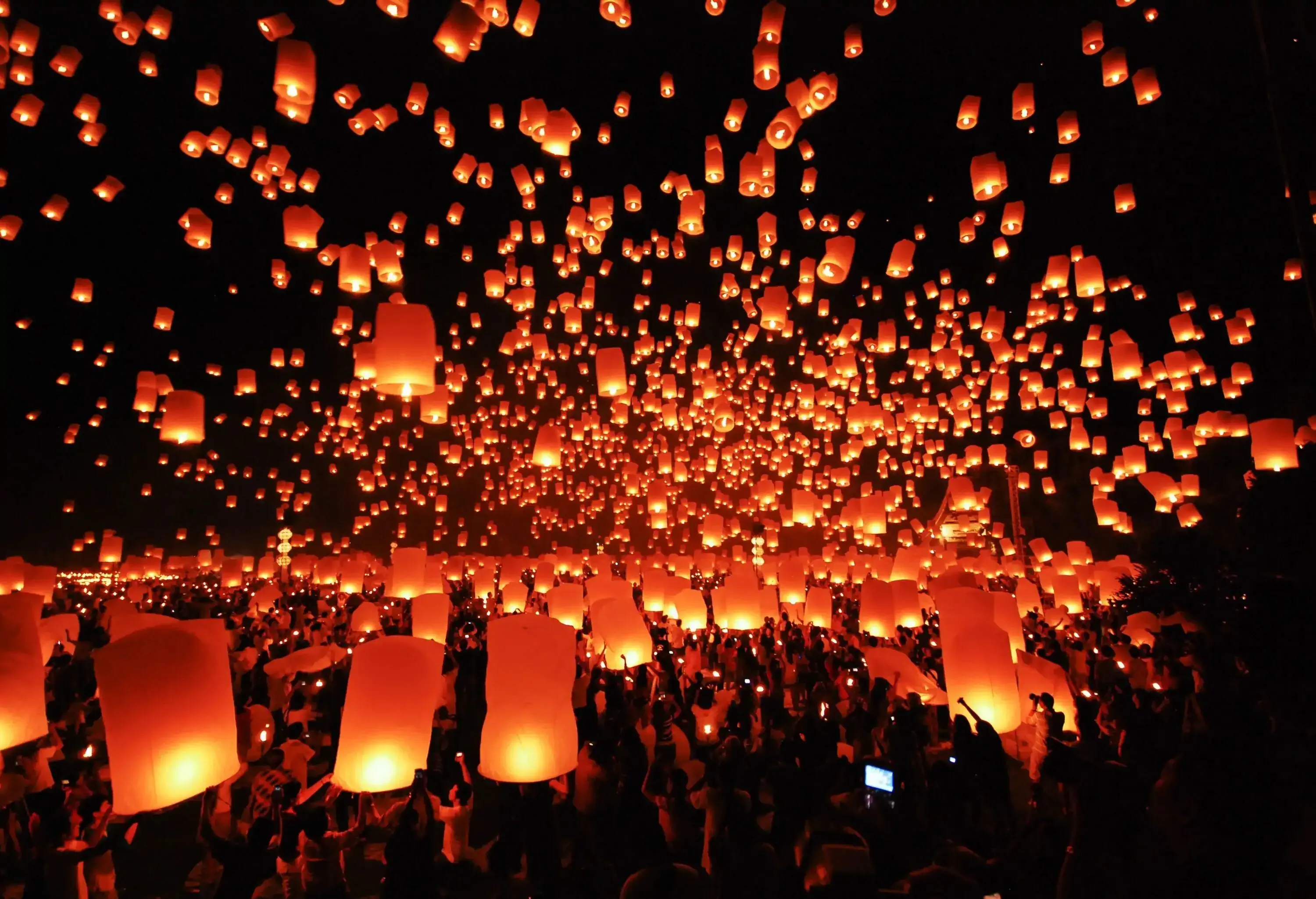 A large crowd raising lit paper lanterns in the air to release them into the night sky.