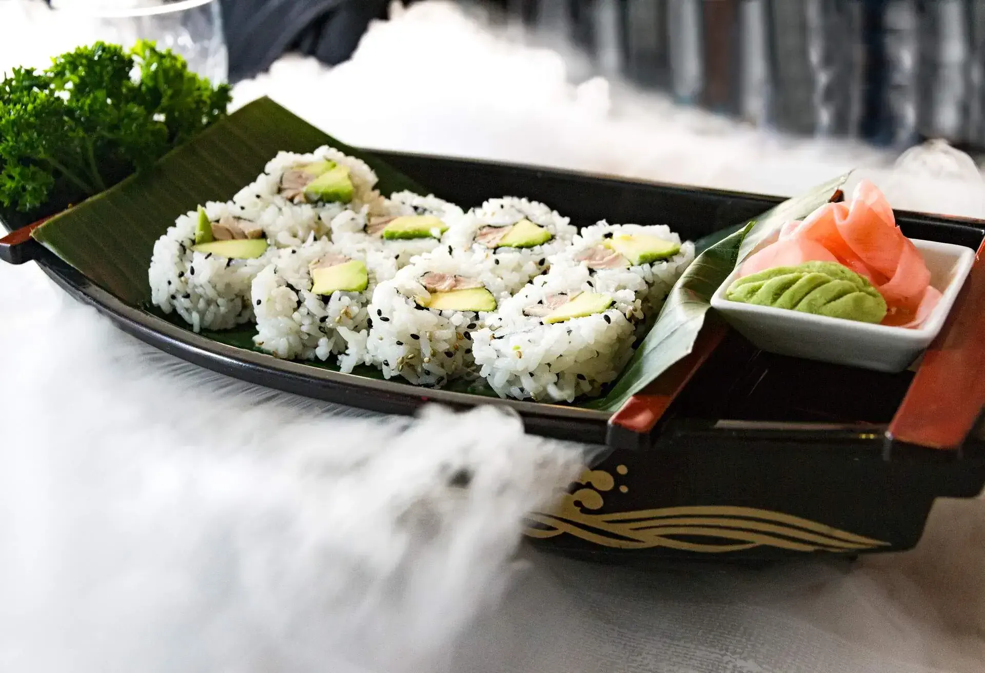 Sushi rolls with rice presented with dry ice in a black boat bowl. Japanese food.