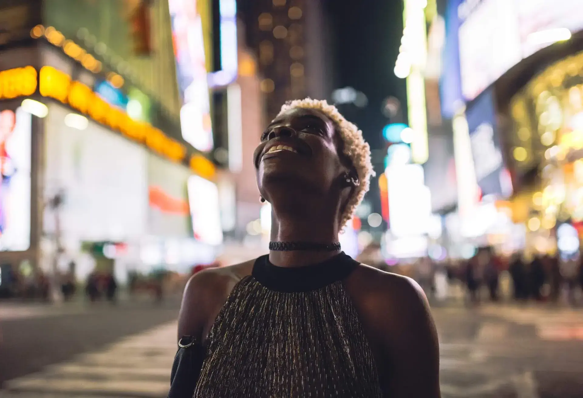 An individual wearing a stylish halter-neck blouse stands in awe, gazing upward as they marvel at the captivating sights on the bustling street.