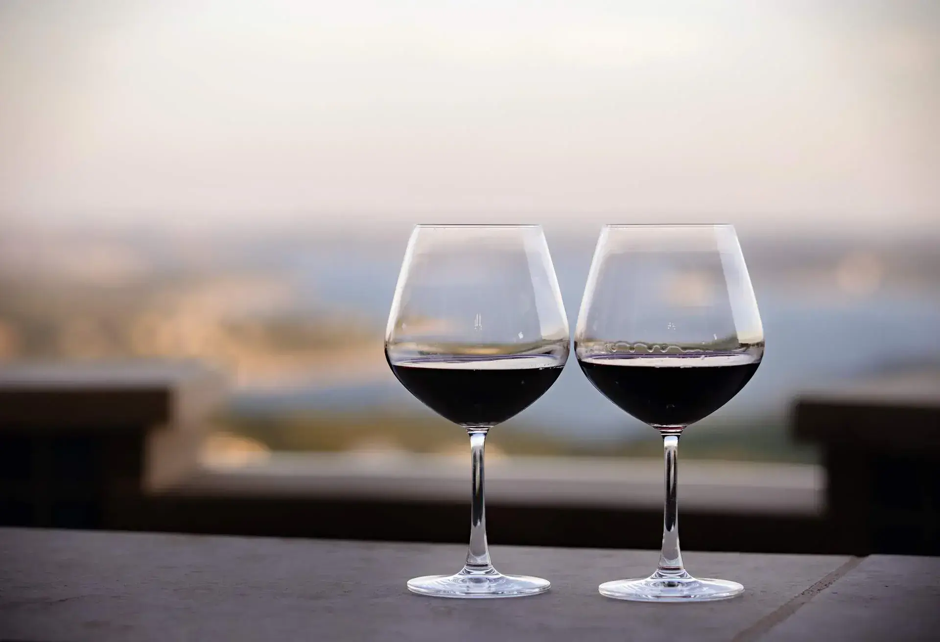 Two Red Wine Glasses side by side on a table with a view overlooking a lake