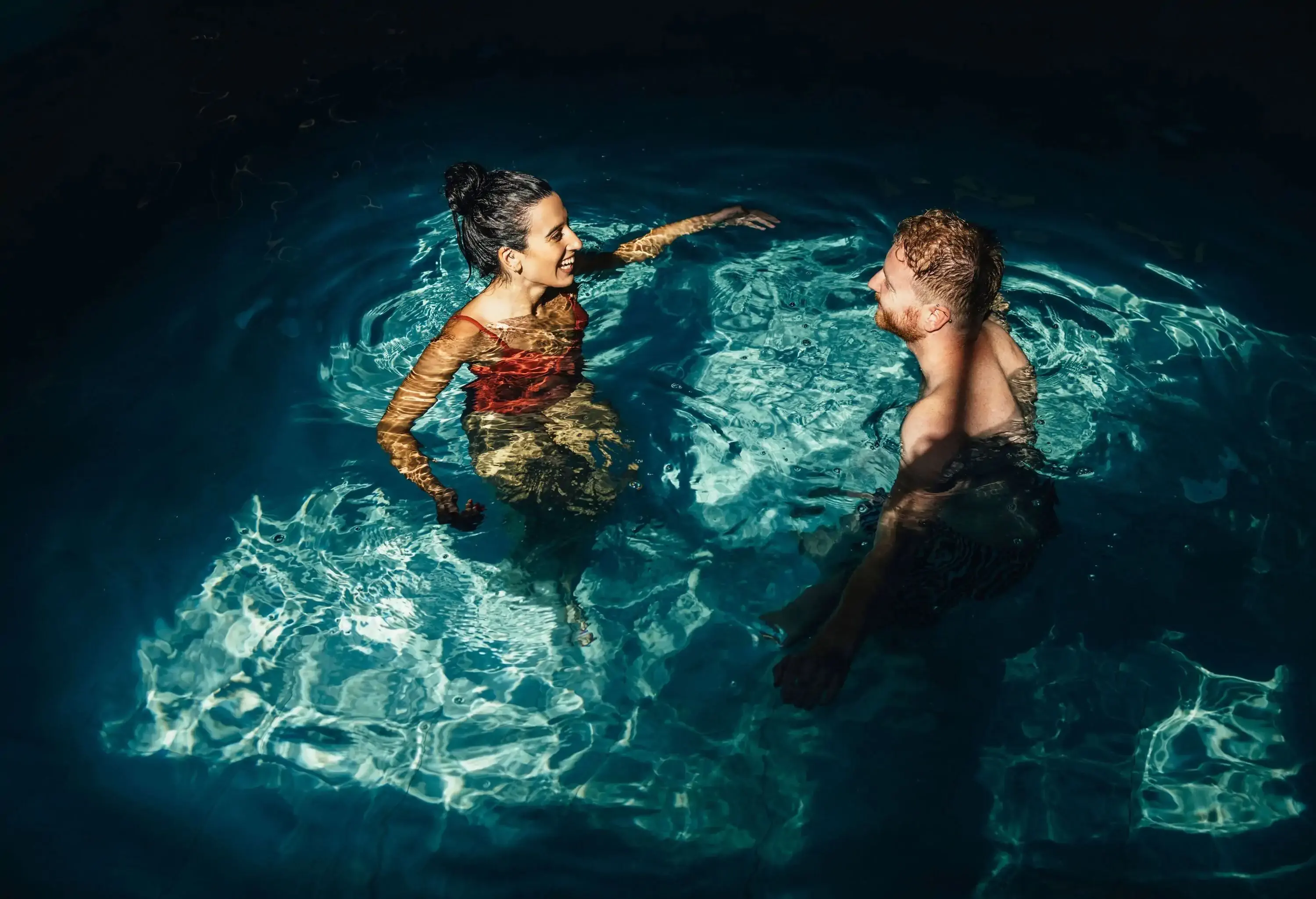 Smiling girlfriend and boyfriend in swimwear talking together in the swimming pool