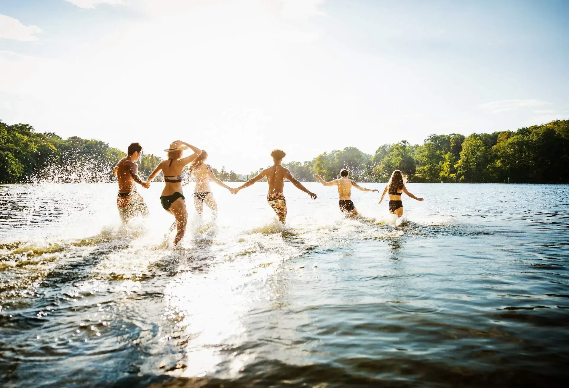 A group of friends wading into lake together in the afternoon summer sun.