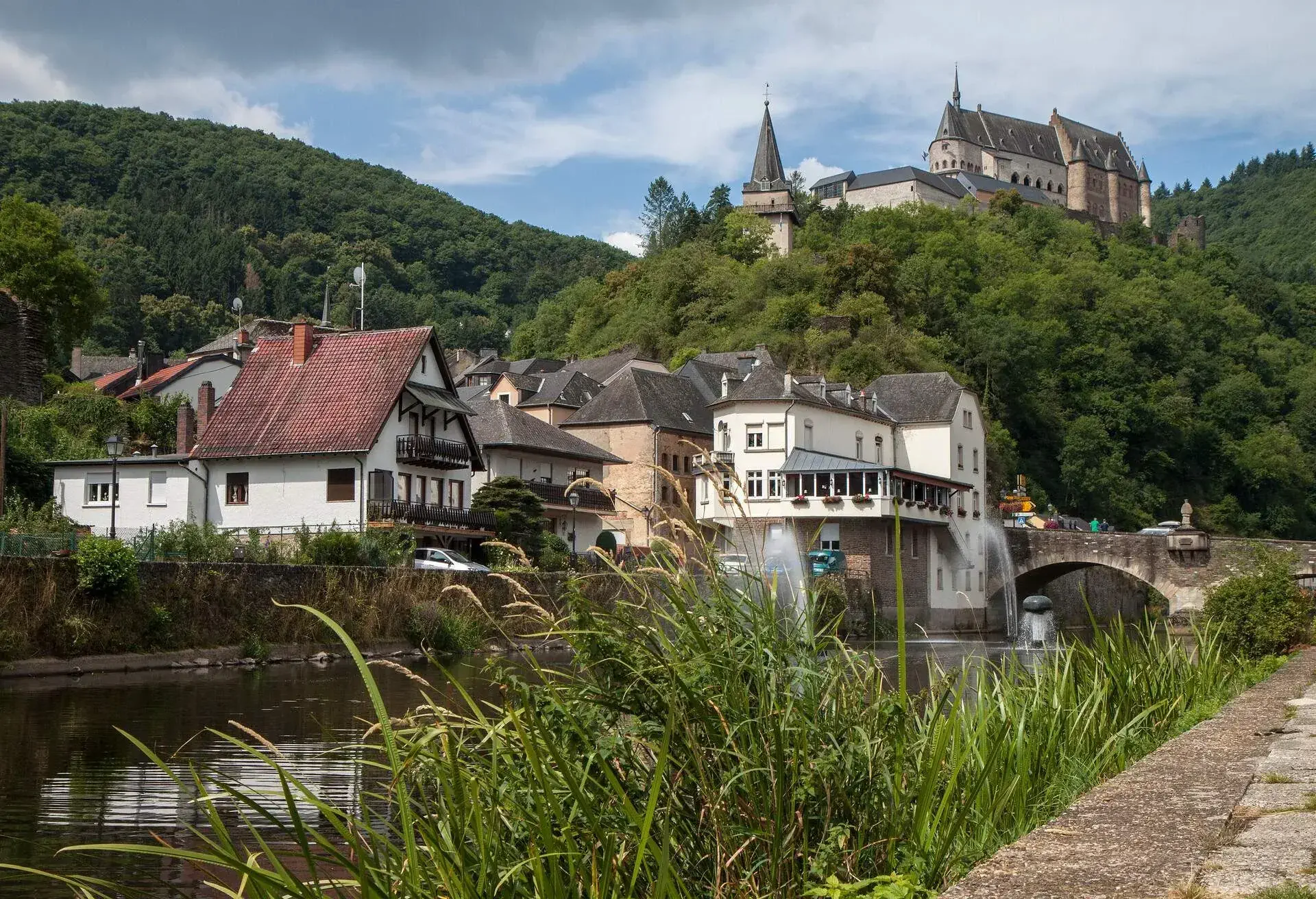 Low angle view of the town, Our River and castle of Vianden, a small country village in the Ardennes region of Luxembourg. The castle sits on a green hill in the background.