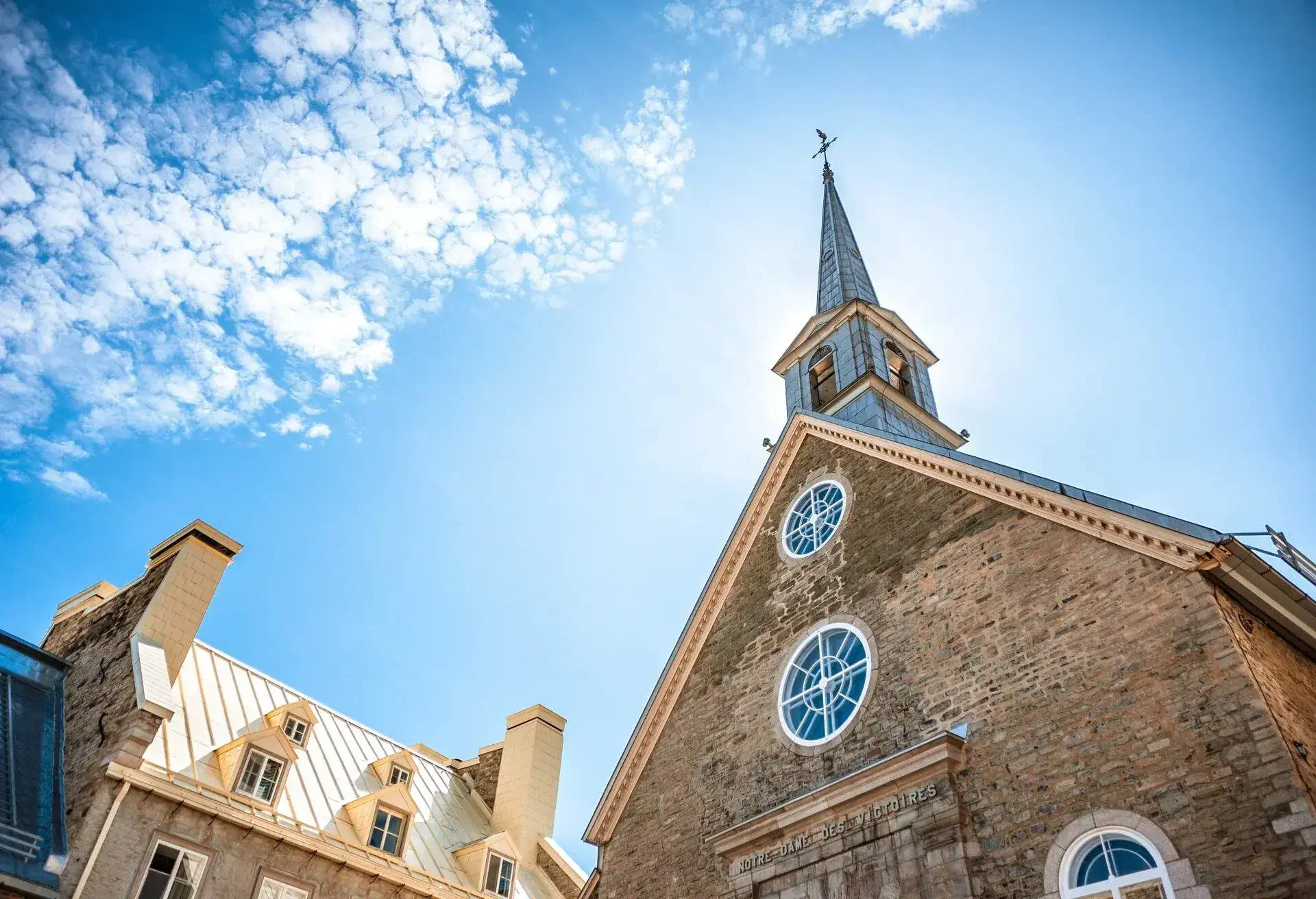Québec City, Québec, Canada - September 1st, 2019: A low angle view of the Notre-Dame-des-Victoires church in the old Québec City with classic French-Canadian colonial style buildings against a sunny clear blue sky.