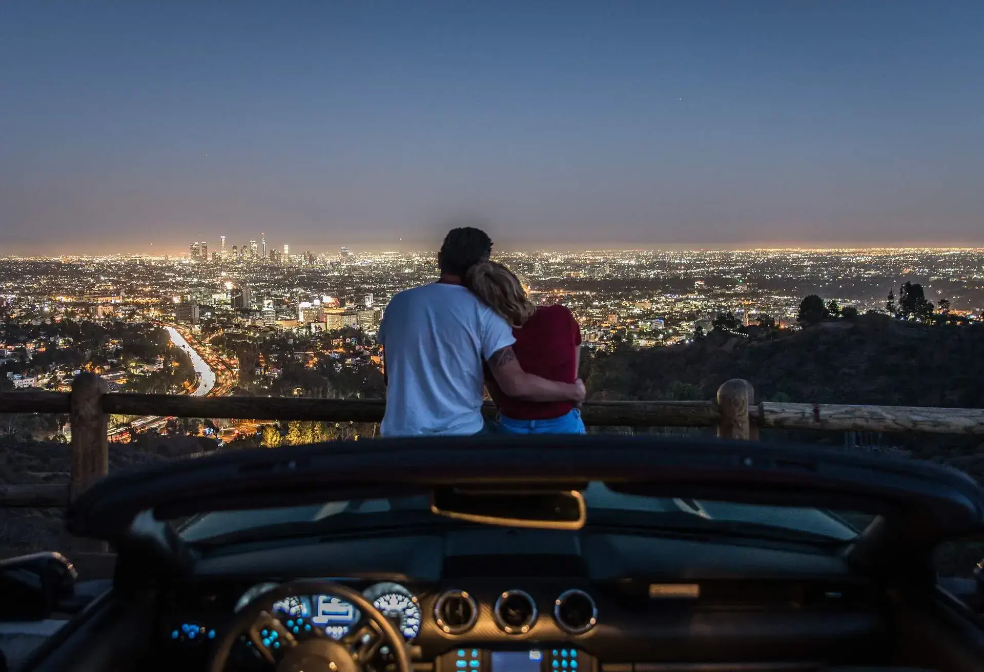 Sweet couple sitting on the hood of a car, taking in the nighttime beauty of the city.