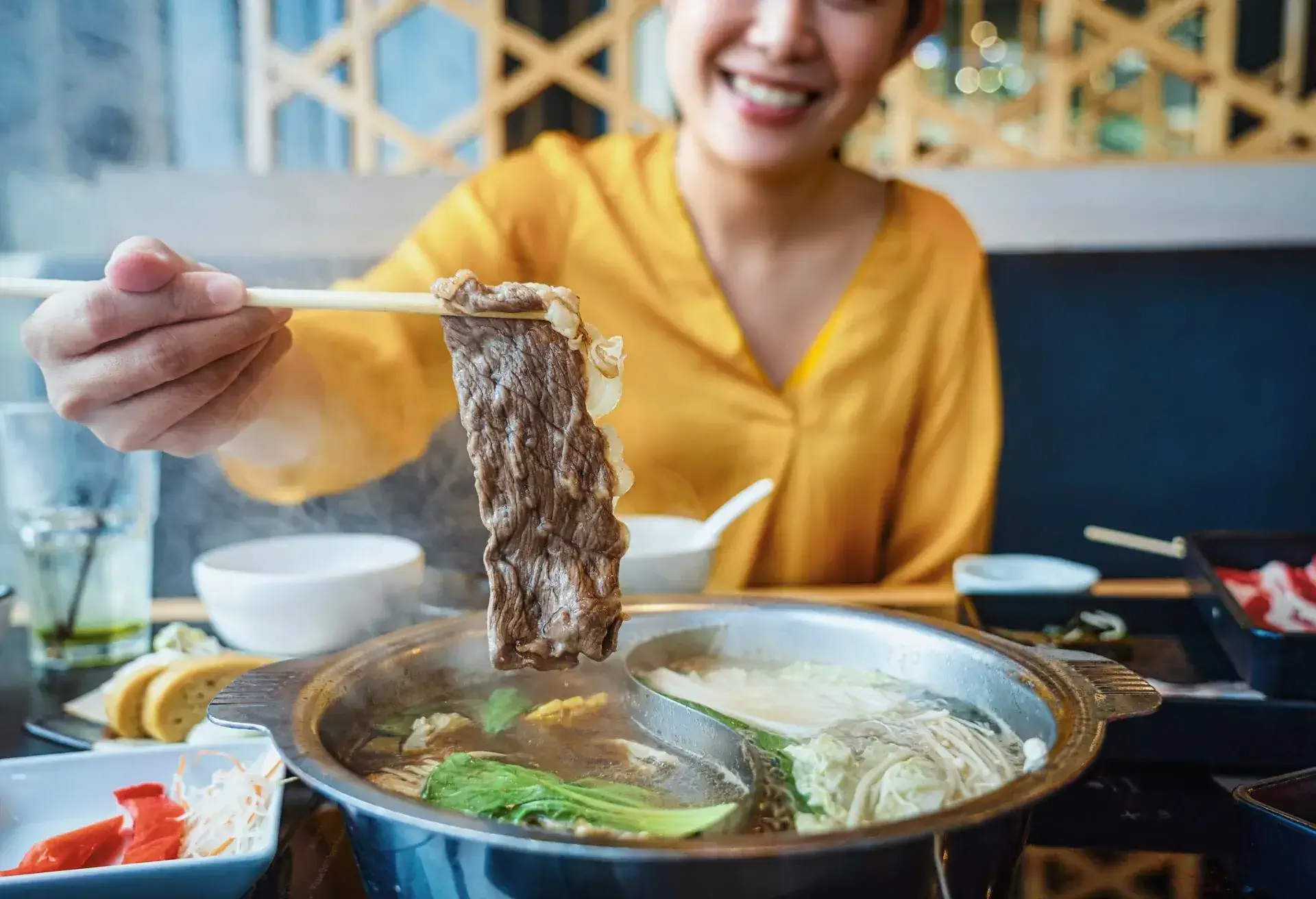 Attraction Asian woman using chopsticks to Dipping the slice of beef into shabu hot pot in the hotel. for social media or vlogger influencer, lifestyle and food concept